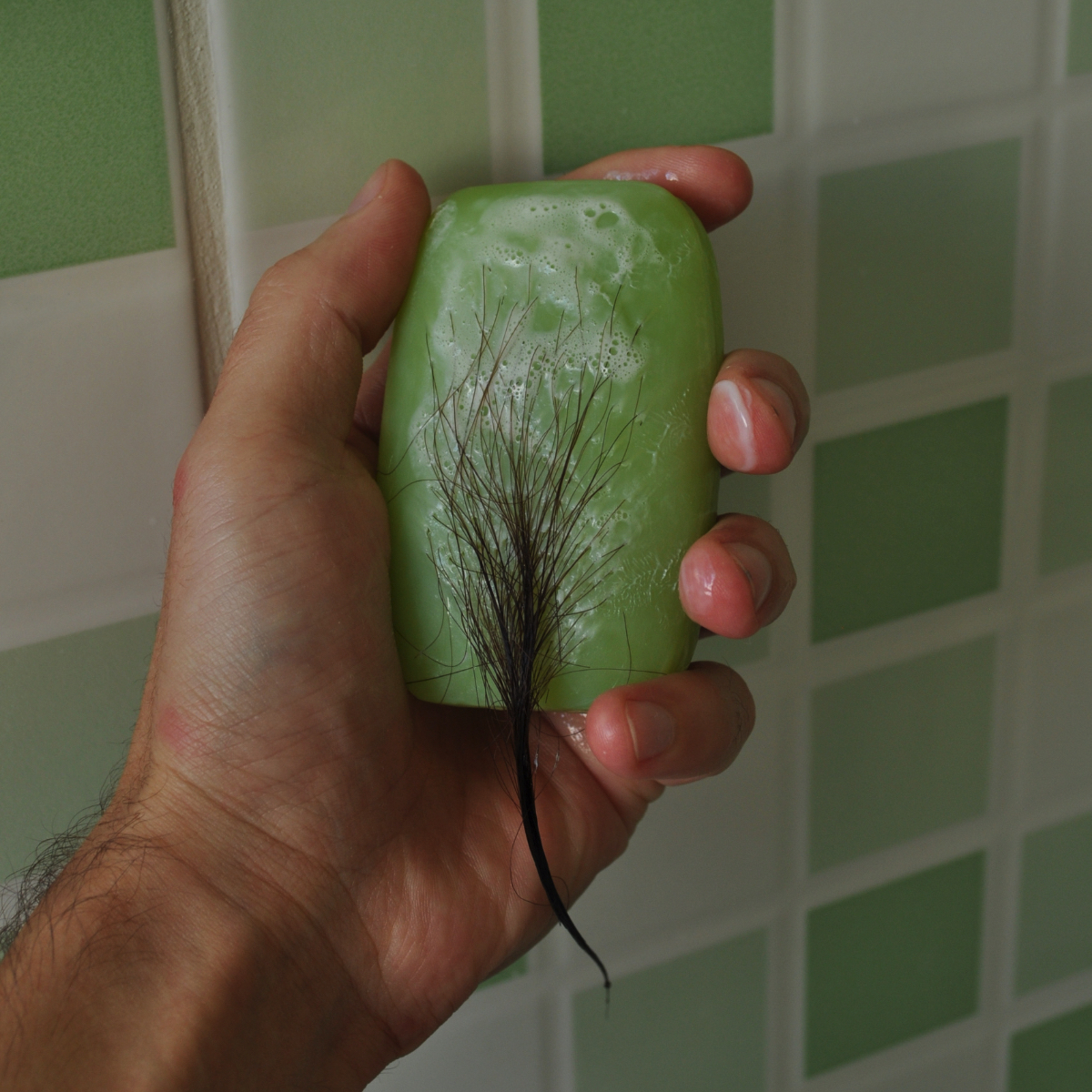 Matteo Ingrao, sculpture, art - Photo of human hand holding up green bar of soap, soap is covered in black hair.