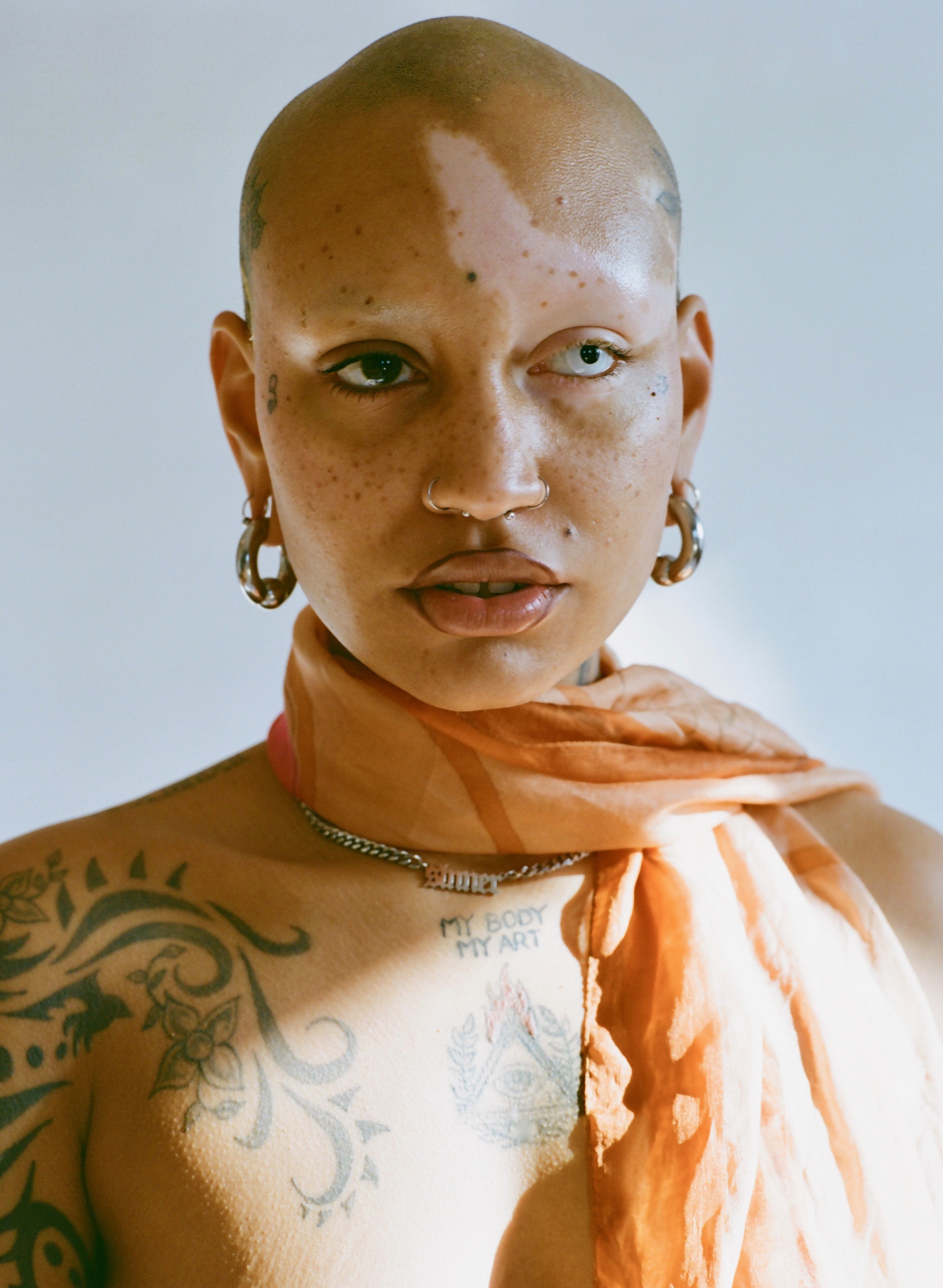 Portrait of a model with tattoos on body, an orange scarf and chain necklace.