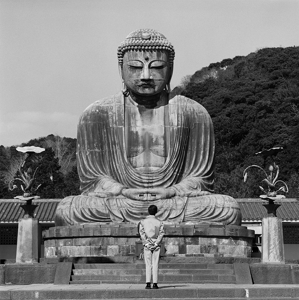a man in a Zhongshan suit stood looking at a buddha sculpture