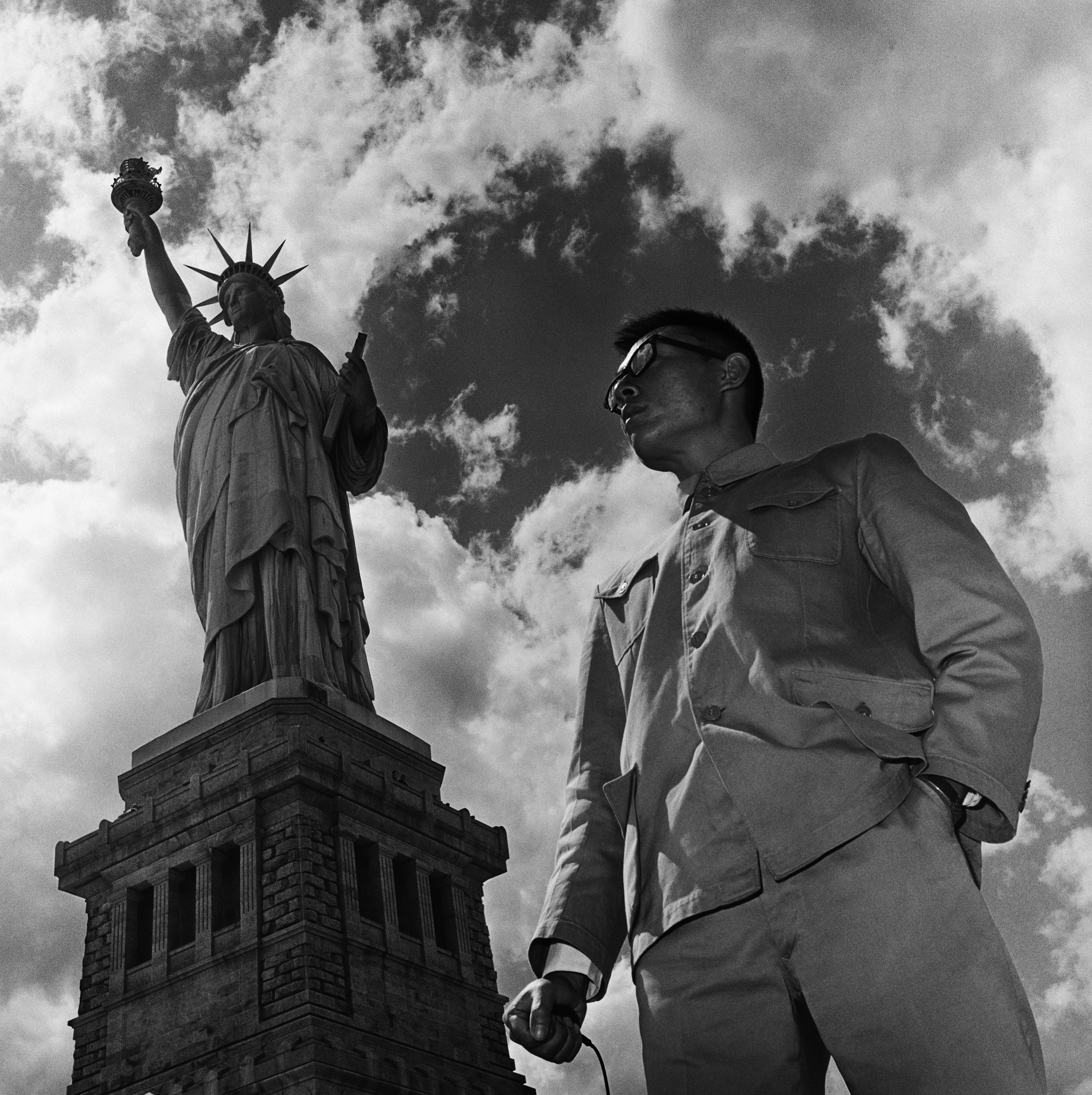  a man in a Zhongshan suit stood in front of the statue of liberty