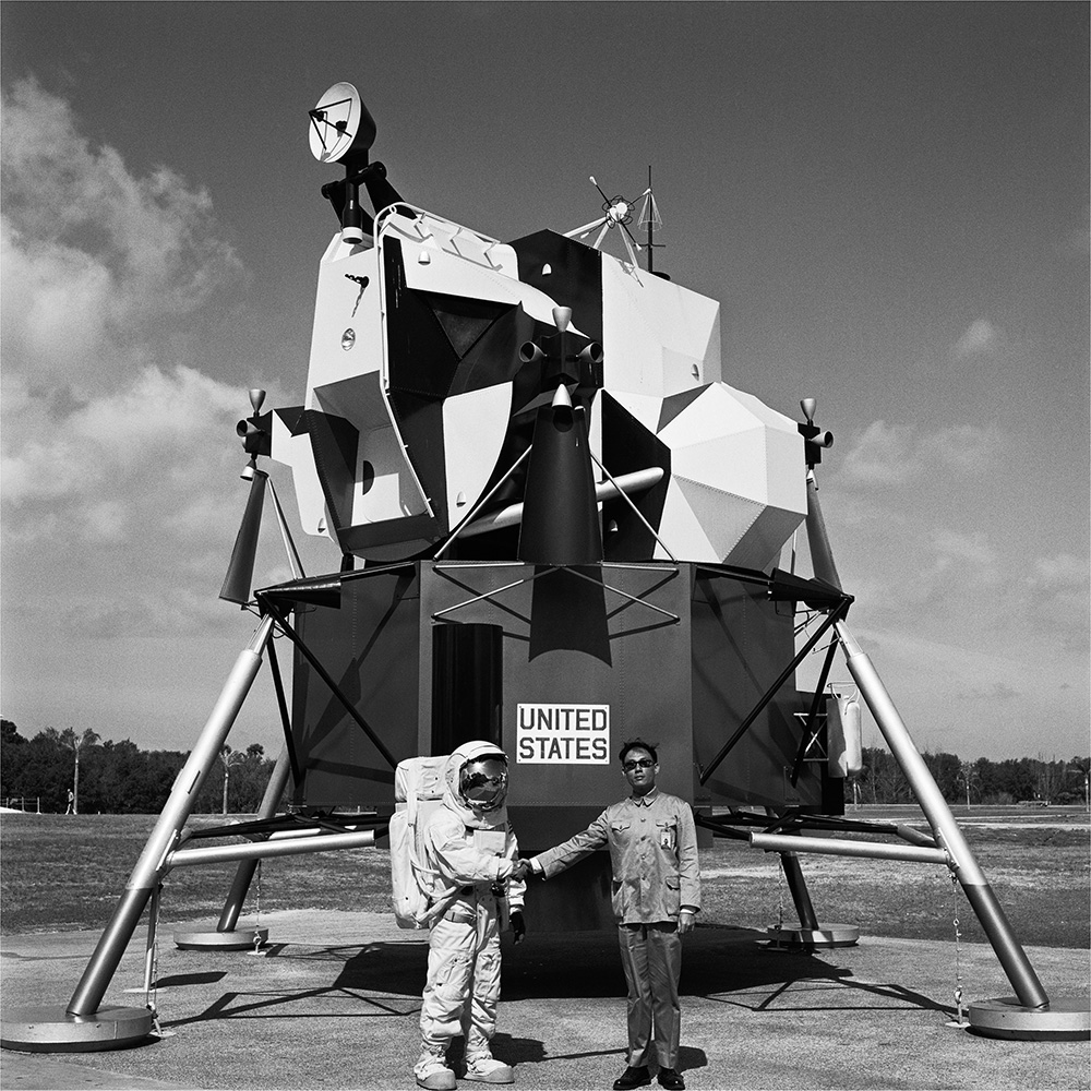  a man in a Zhongshan suit stood in front of a space age structure holding hands with an astronaut