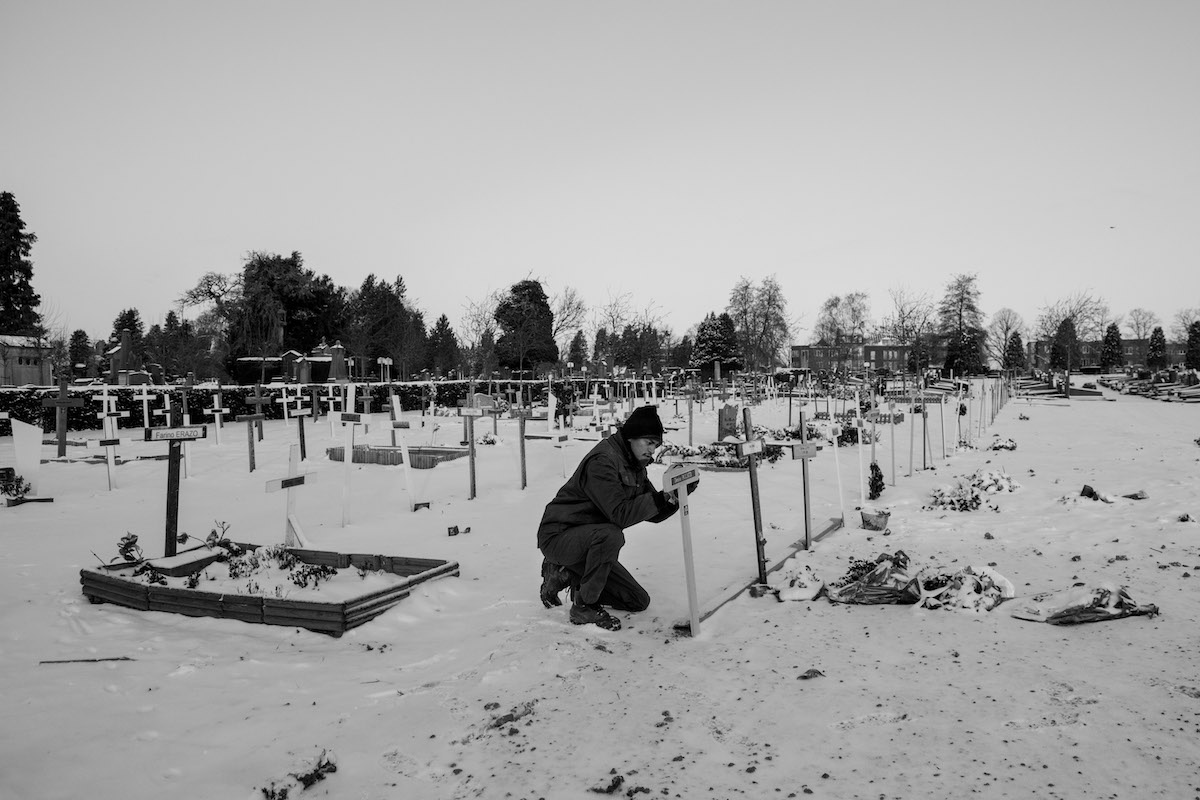 Jacques Vermeer, Patrick, cemetery - Black and white photo of a man in a hat tending to a snow covered graveyard.