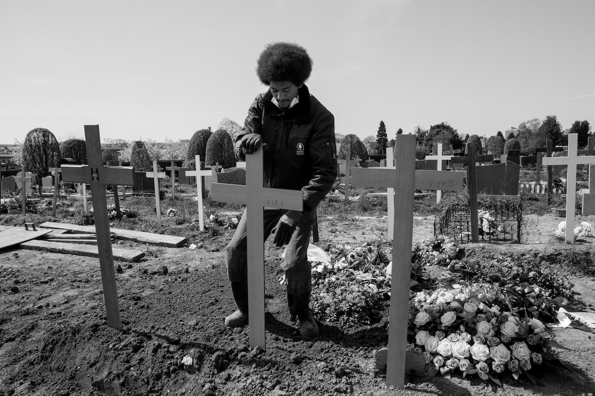 Jacques Vermeer, Patrick, cemetery - Black and white photo of a man tending to a cross in a cemetery on a sunny day.