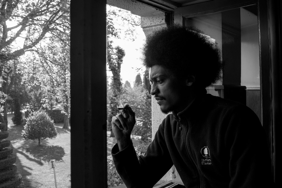 Jacques Vermeer, Patrick, cemetery - Black and white photo of a man with an afro and a cigarette looking out of a window.