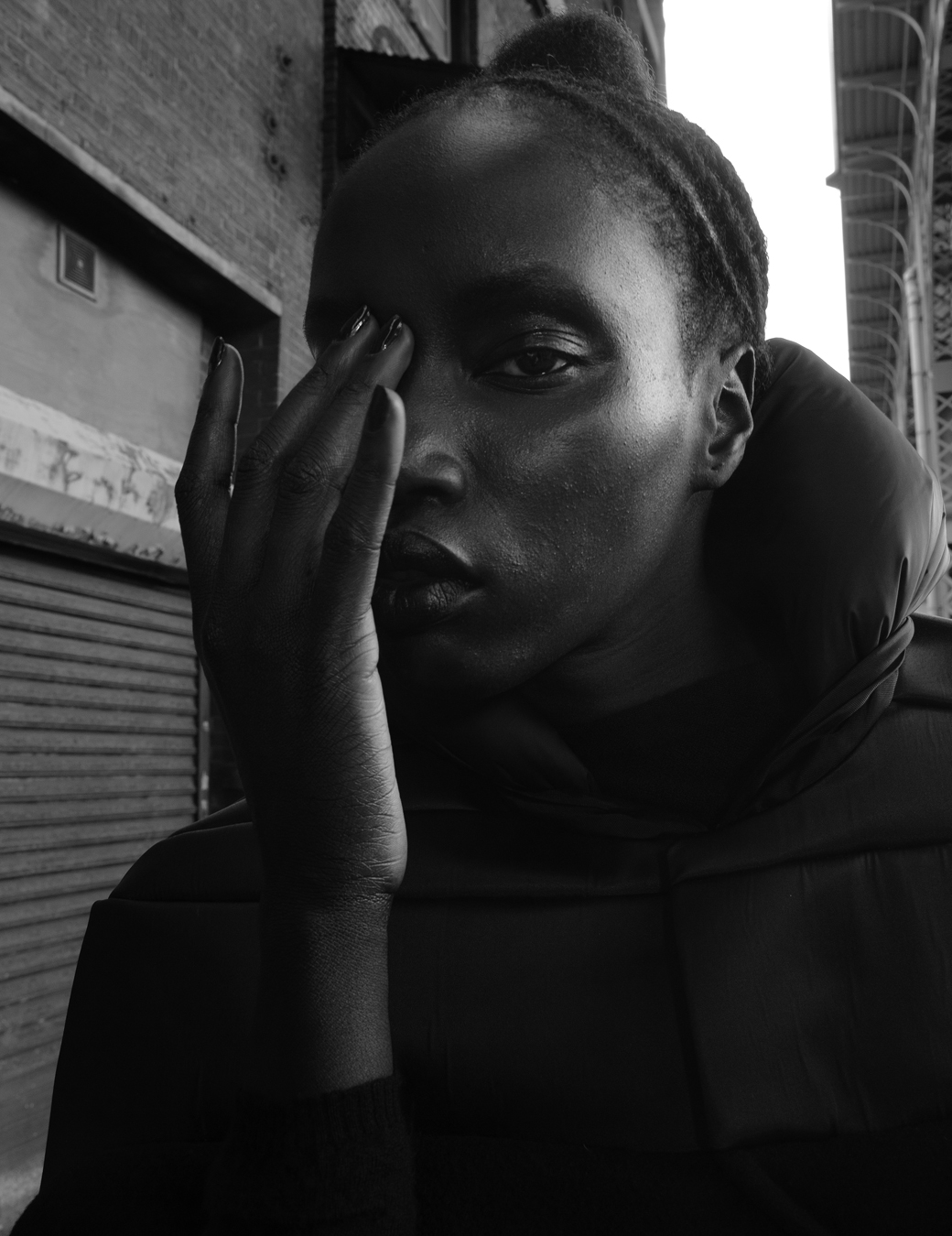 Anok Yai wears a black puffer hoodie and cat ears next to a garage door