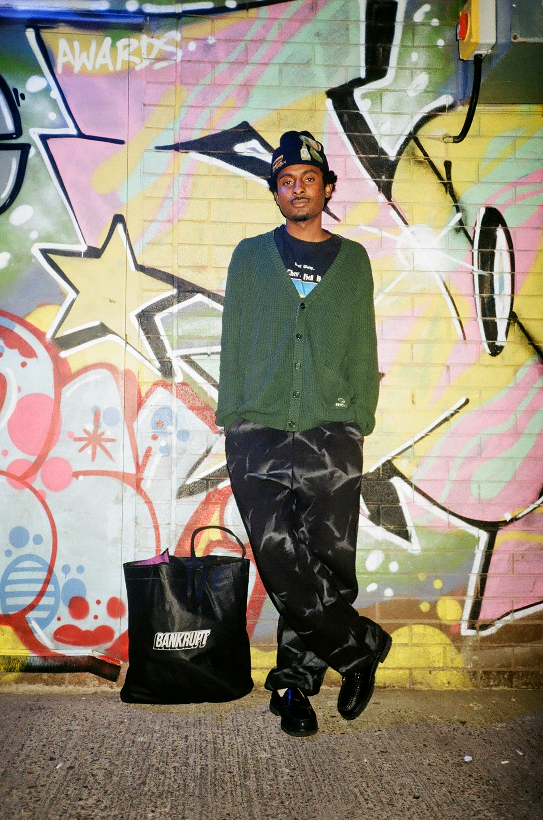 a young man wearing slouches against a colourful wall of graffiti
