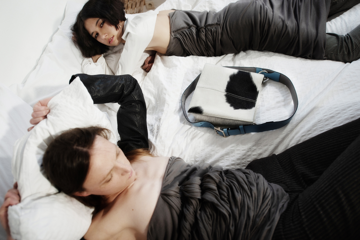 two women lying in bed wearing grey clothes