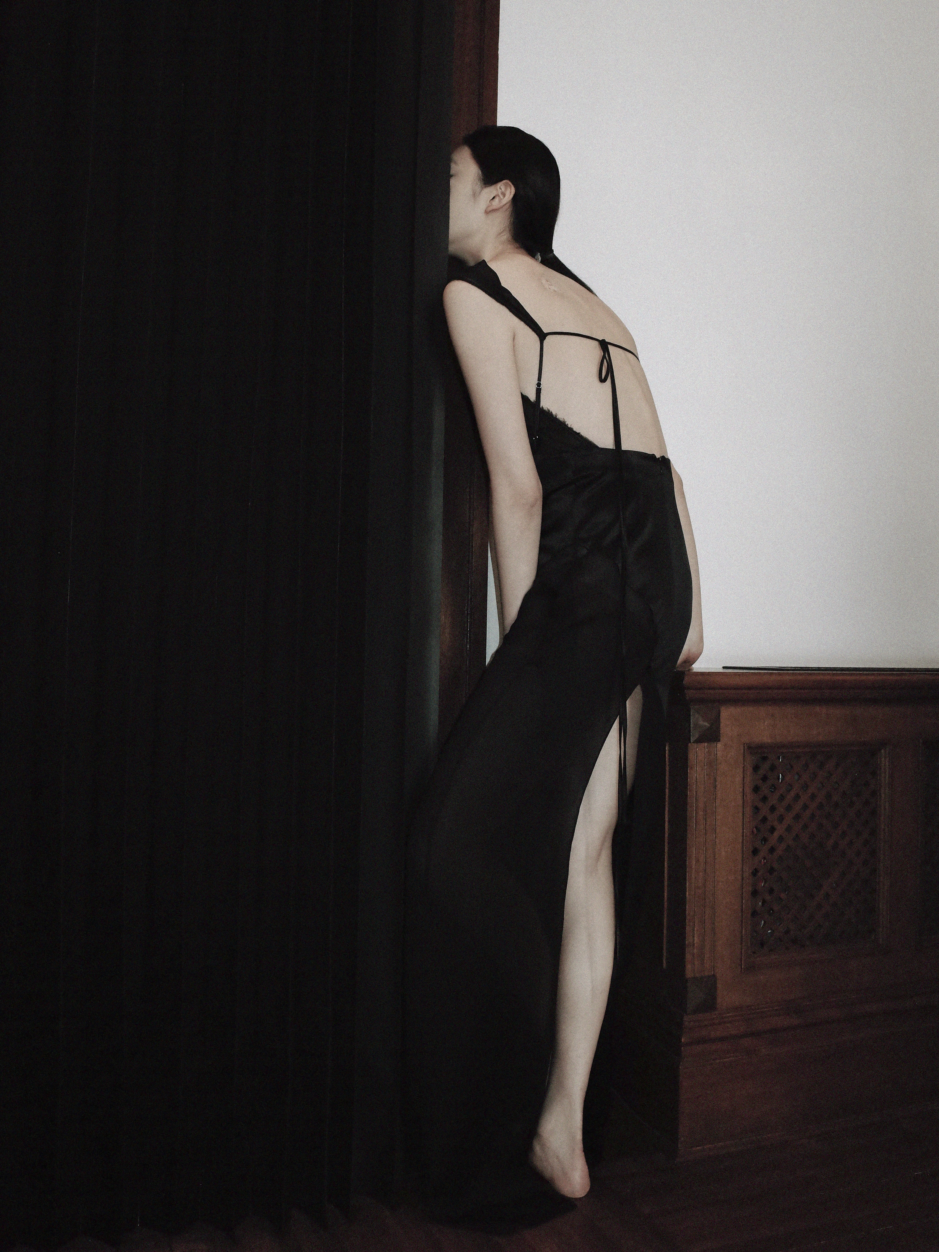 A model wearing a long black Peter Do dress, with her face hid behind a curtain