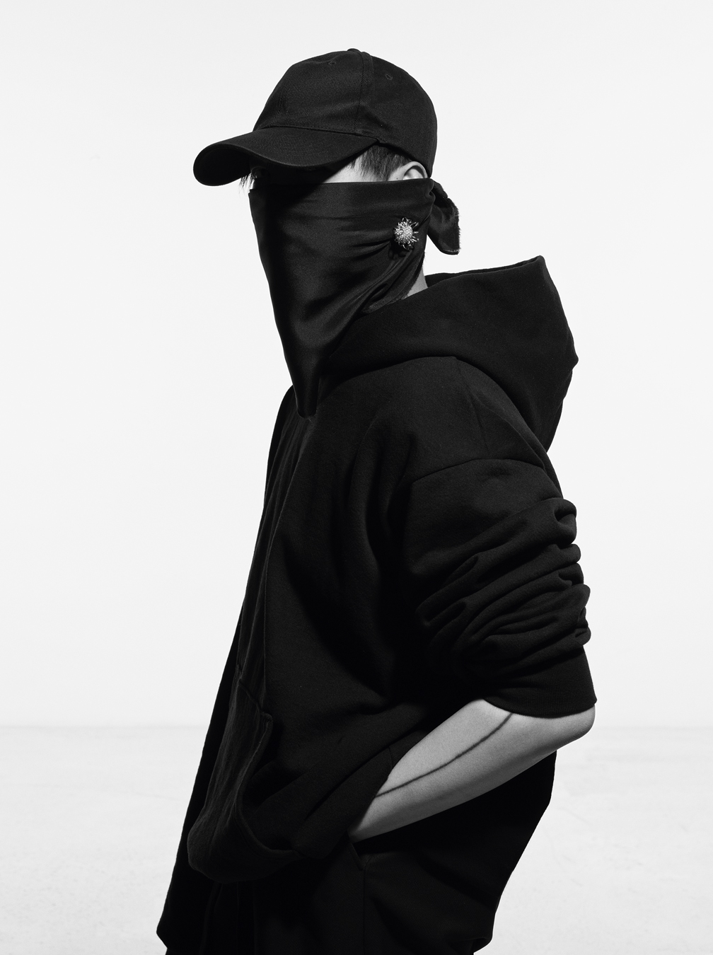 Peter Do wears a black hoodie, a black cap and a black face mask with a diamond embellished jewel on it. 