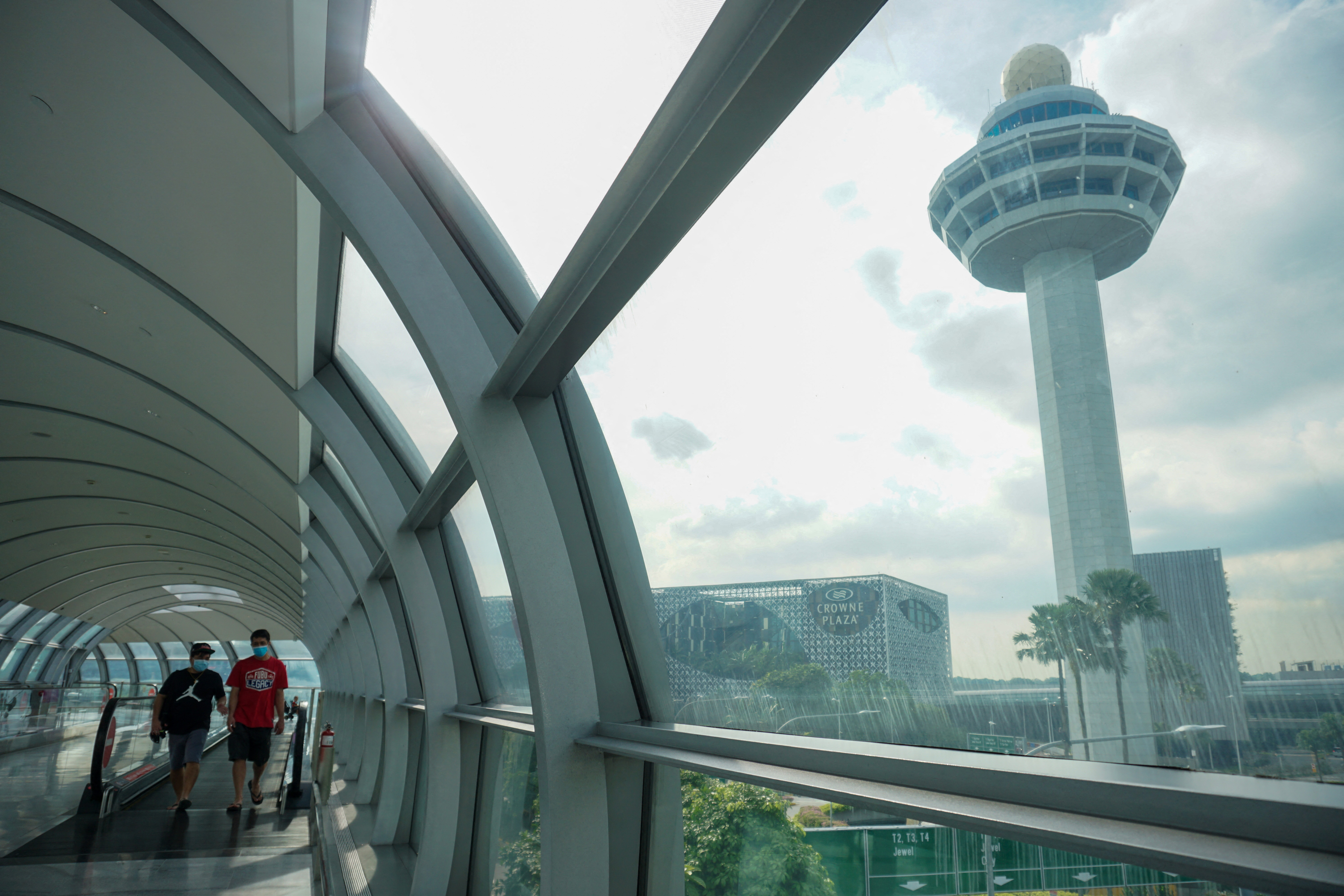 People walk along a link bridge to a terminal at Changi Airport. 