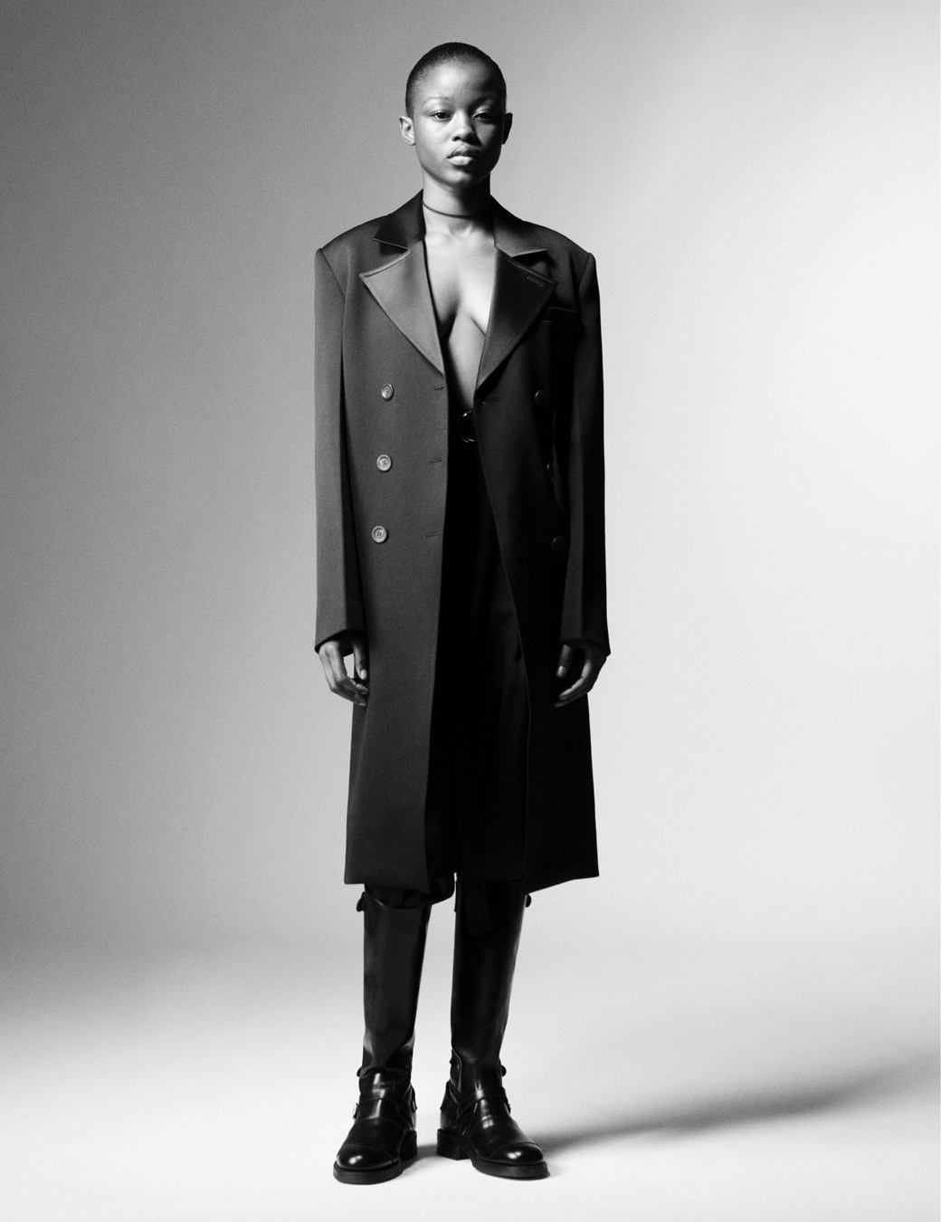 Model wears a black trench coat and black leather boots. 