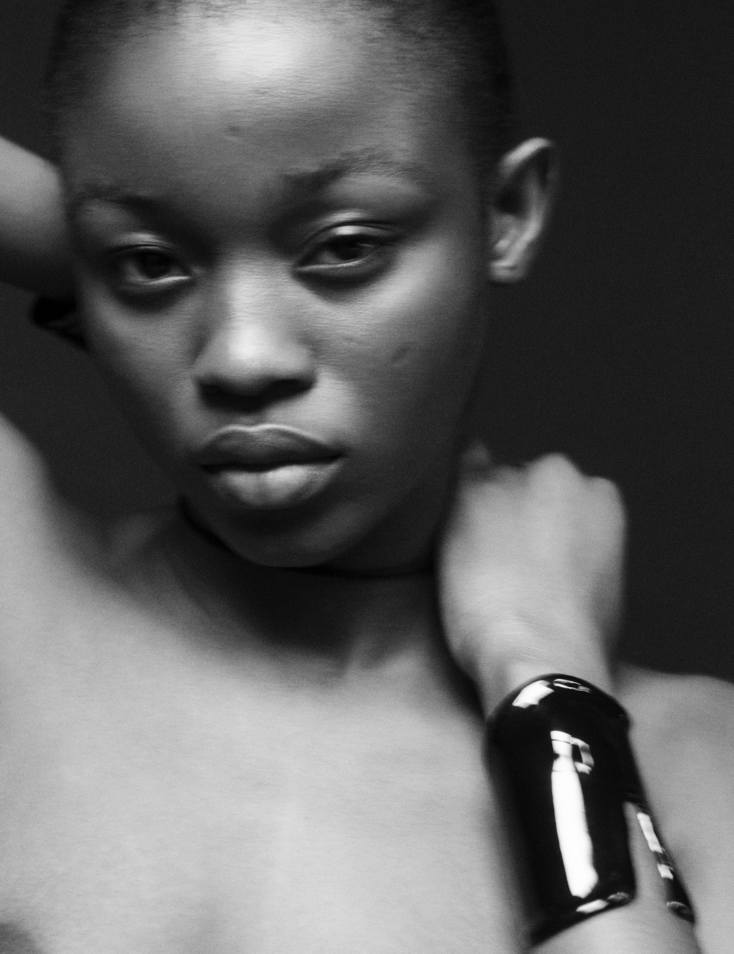 Portrait of model's face wearing a black cuff bracelet. 