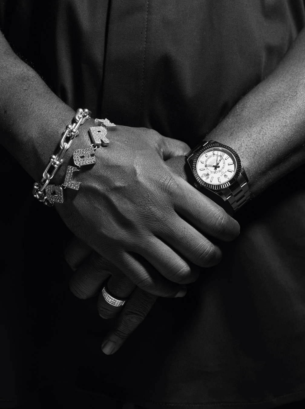 DJ Clark Kent's hands clasped. One with a watch and ring, the other with a chain and diamond CLARK bracelets.