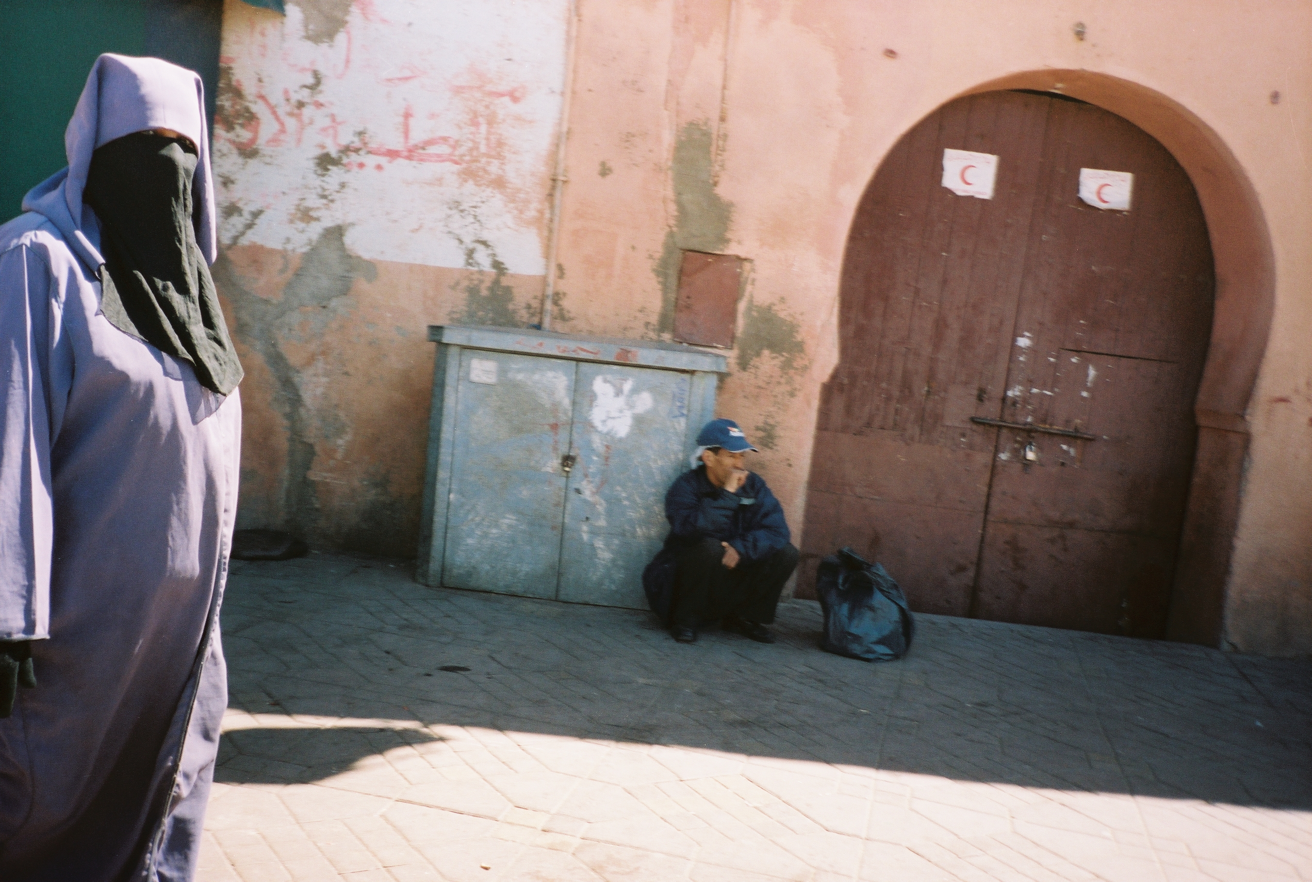 donna con burqa viola e signore seduto per strada