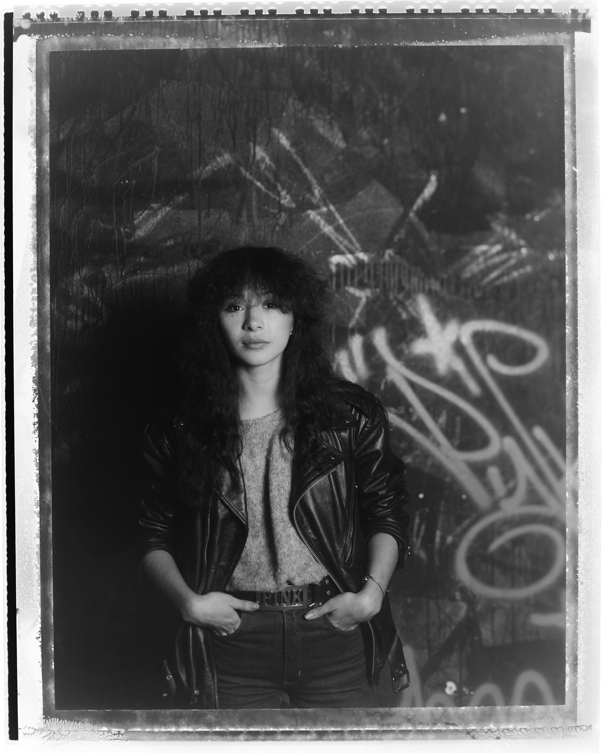 a black and white portrait of Lady Pink in front of graffiti by tom warren