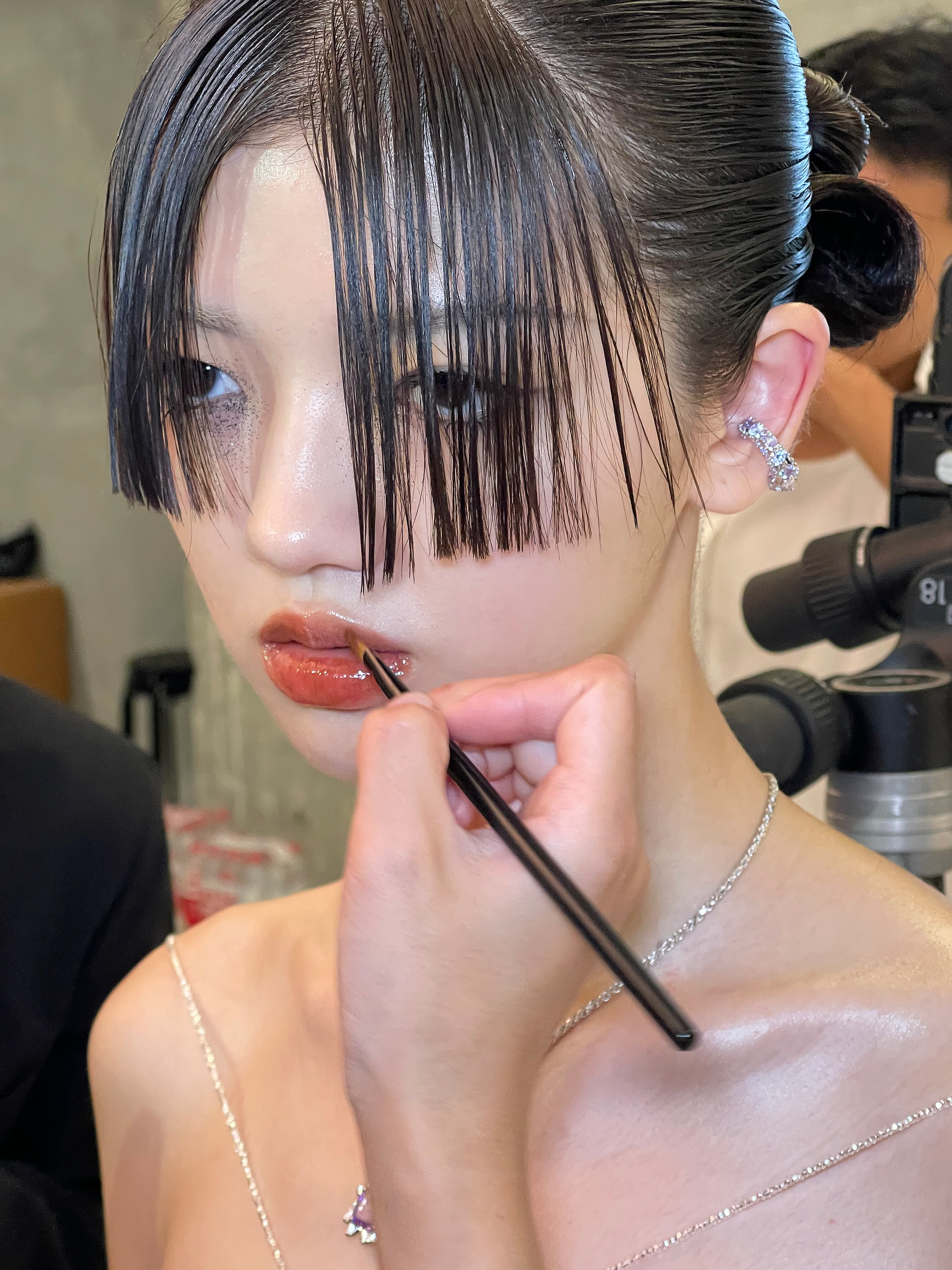a makeup artist applying lip gloss to a model backstage