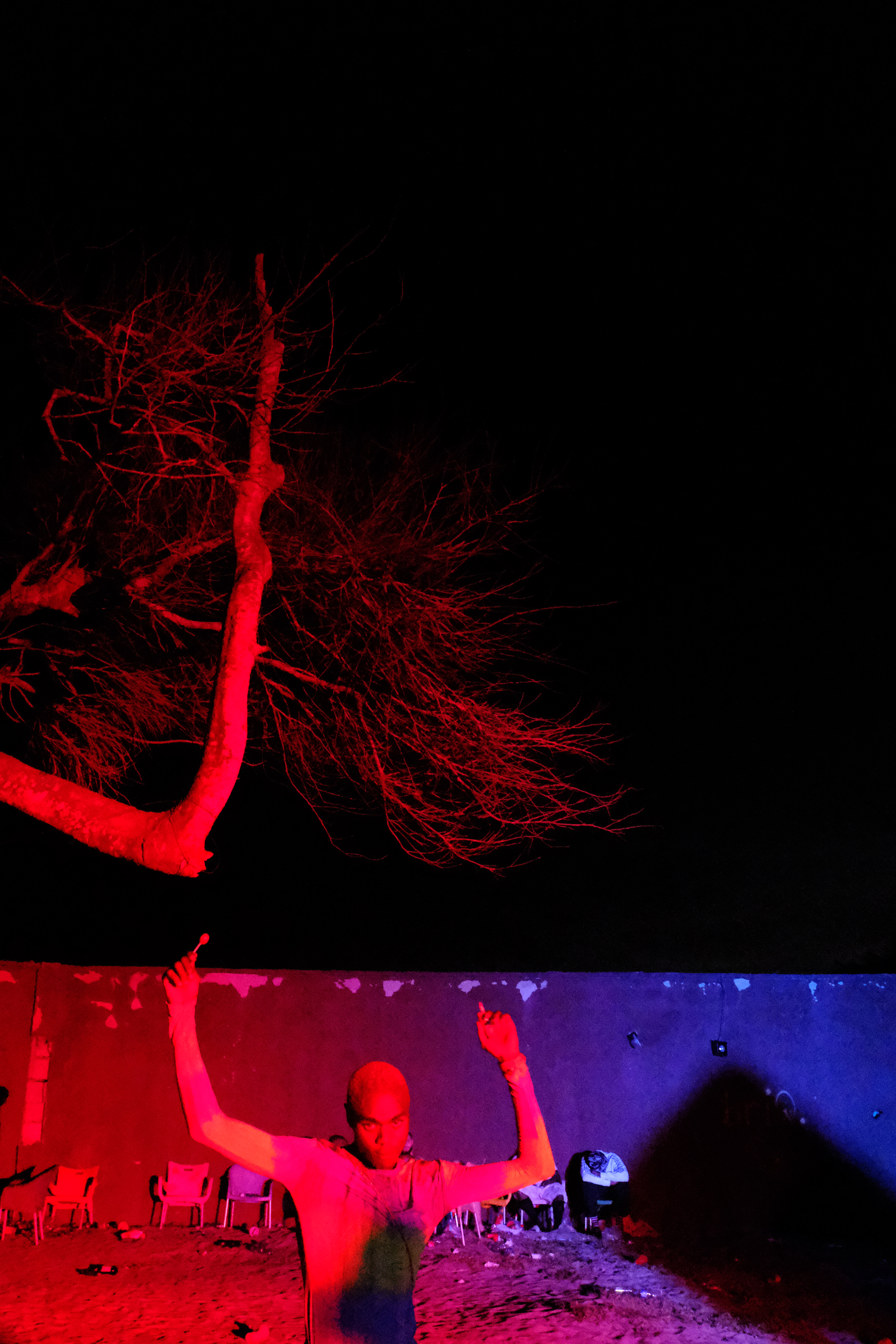 a person dances in an outdoor rave as a red light flashes up the tree