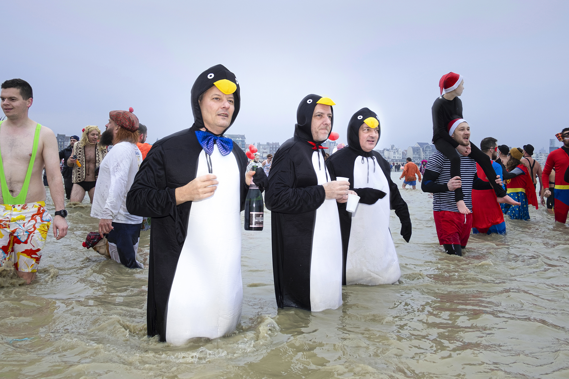 Tiga laki-laki berkostum penguin menyelam di laut