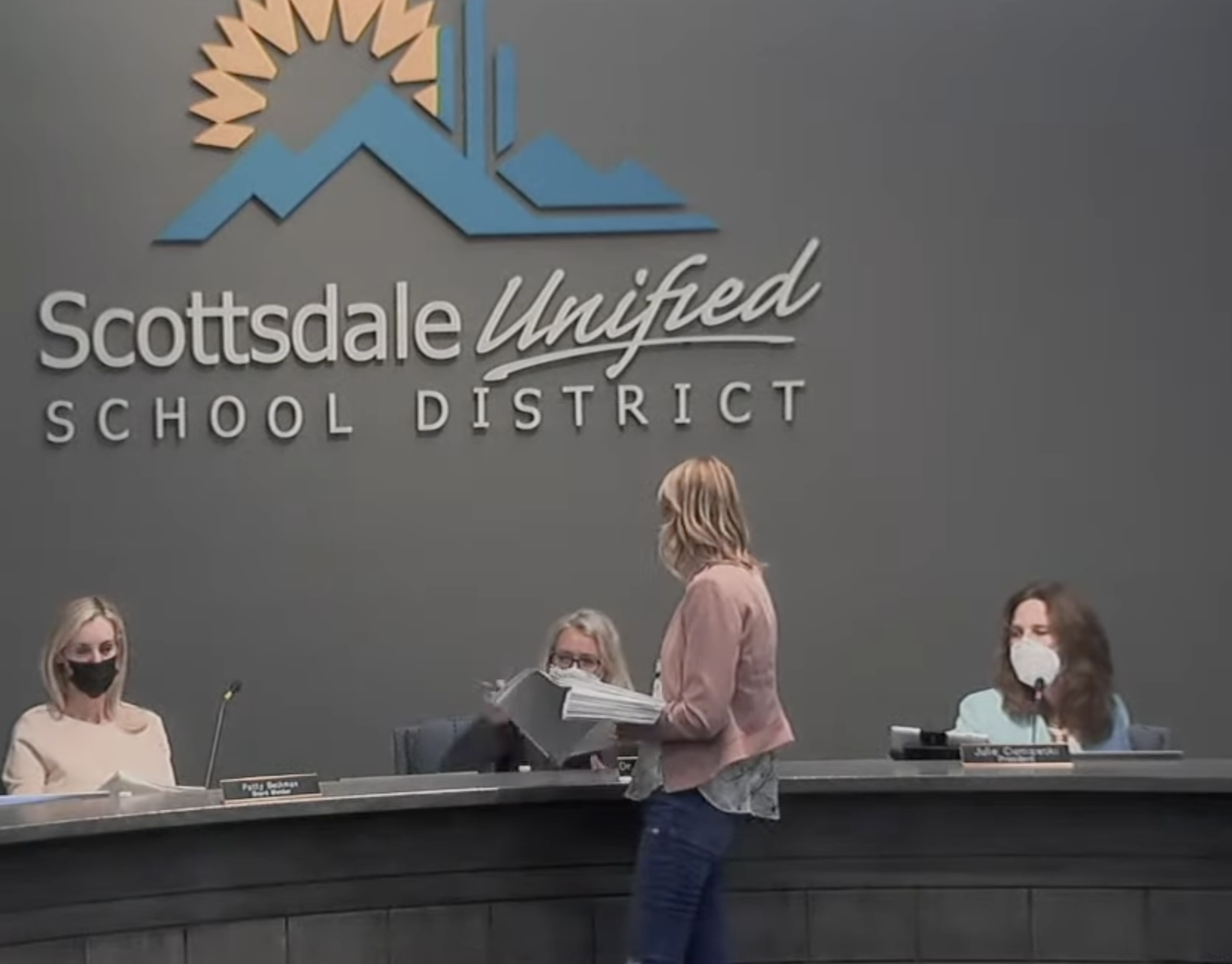 Miki Klann, from “Bonds for the Win”, serving Scottsdale Unified School District board members with documents during a meeting on Tuesday (YouTube/Scottsdale Unified School District)