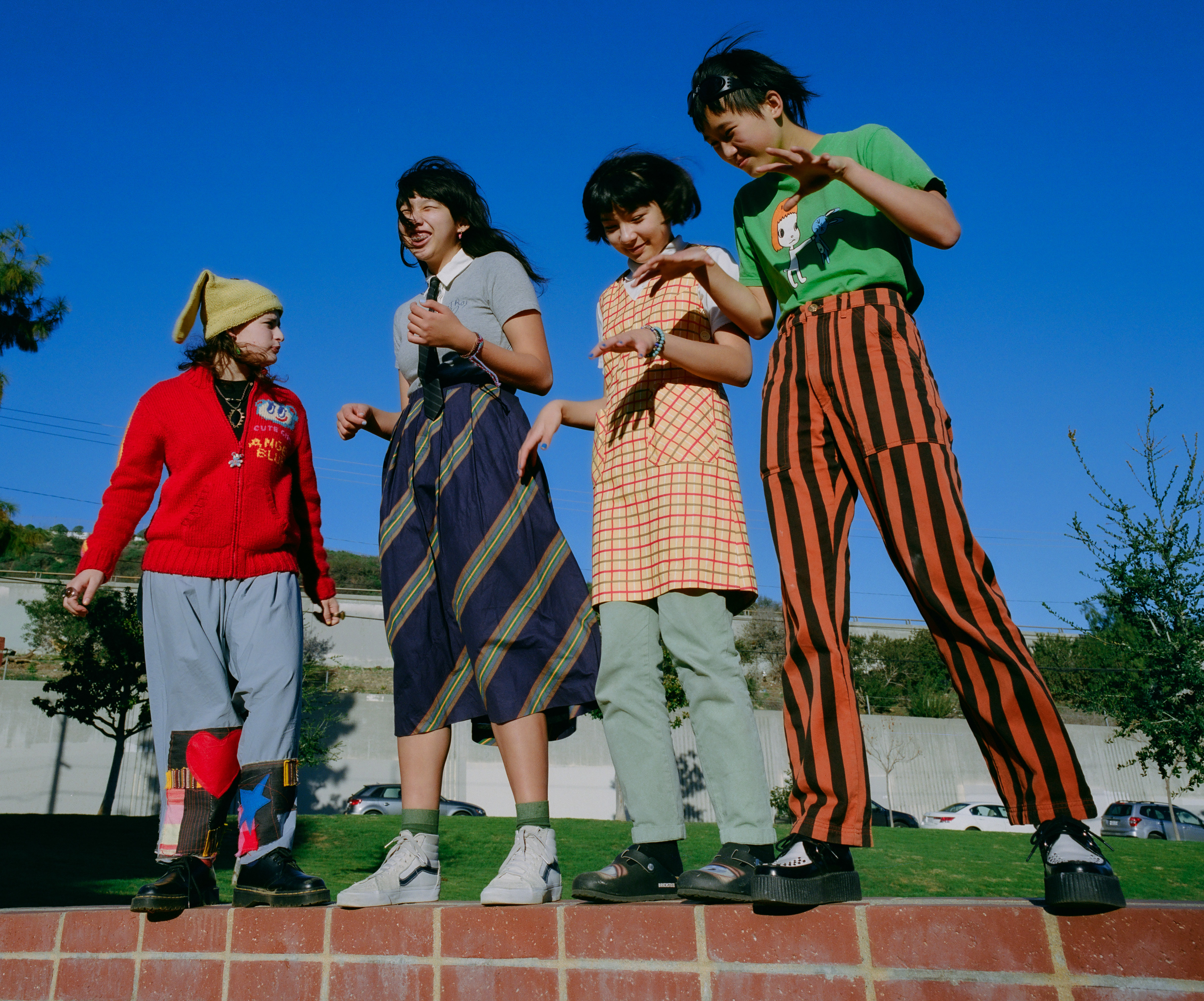 The Linda Lindas stand together wearing colourful clothes against a bright blue sky in LA