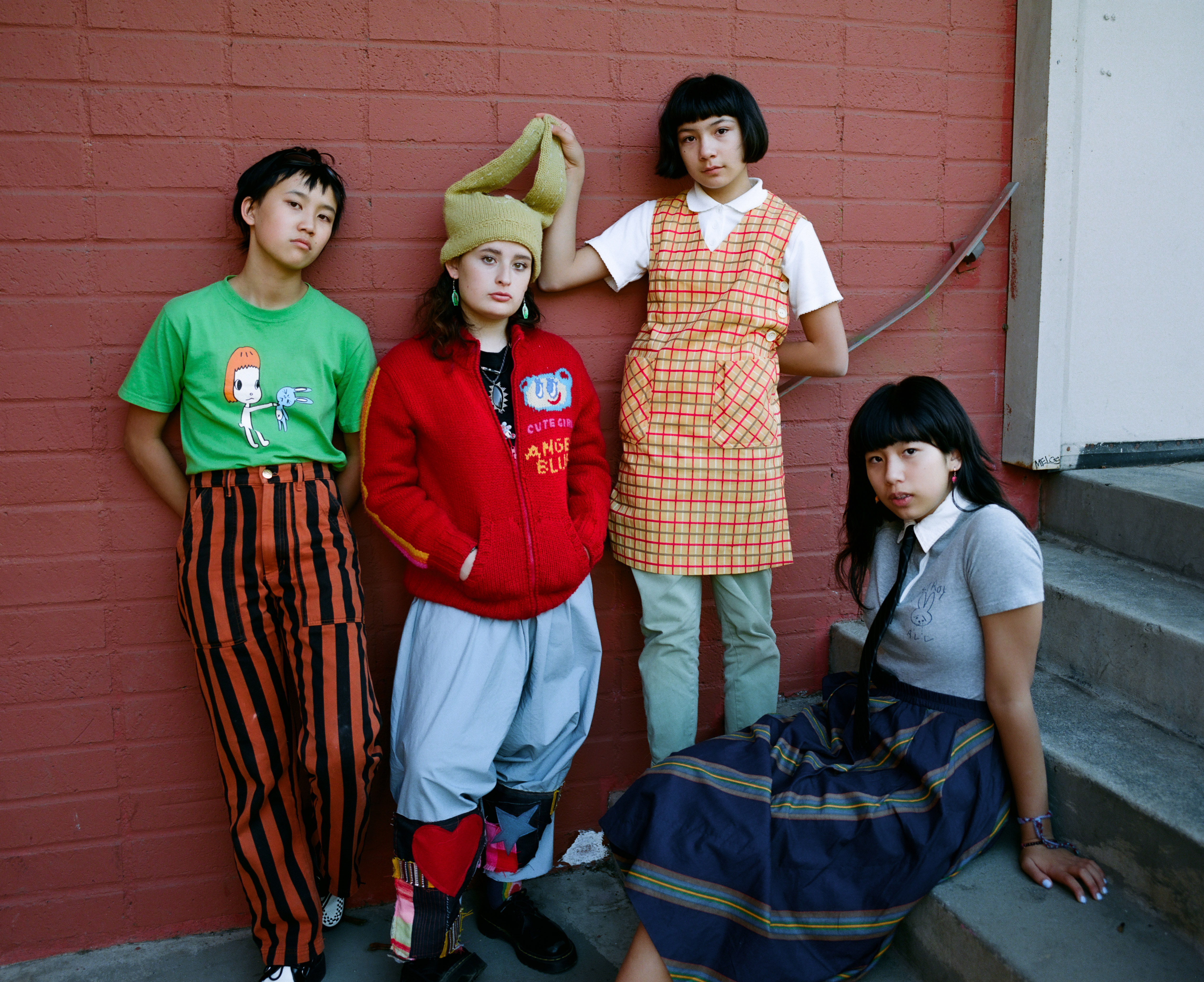 The Linda Lindas hang out on a stairwell wearing colourful 90s clothes