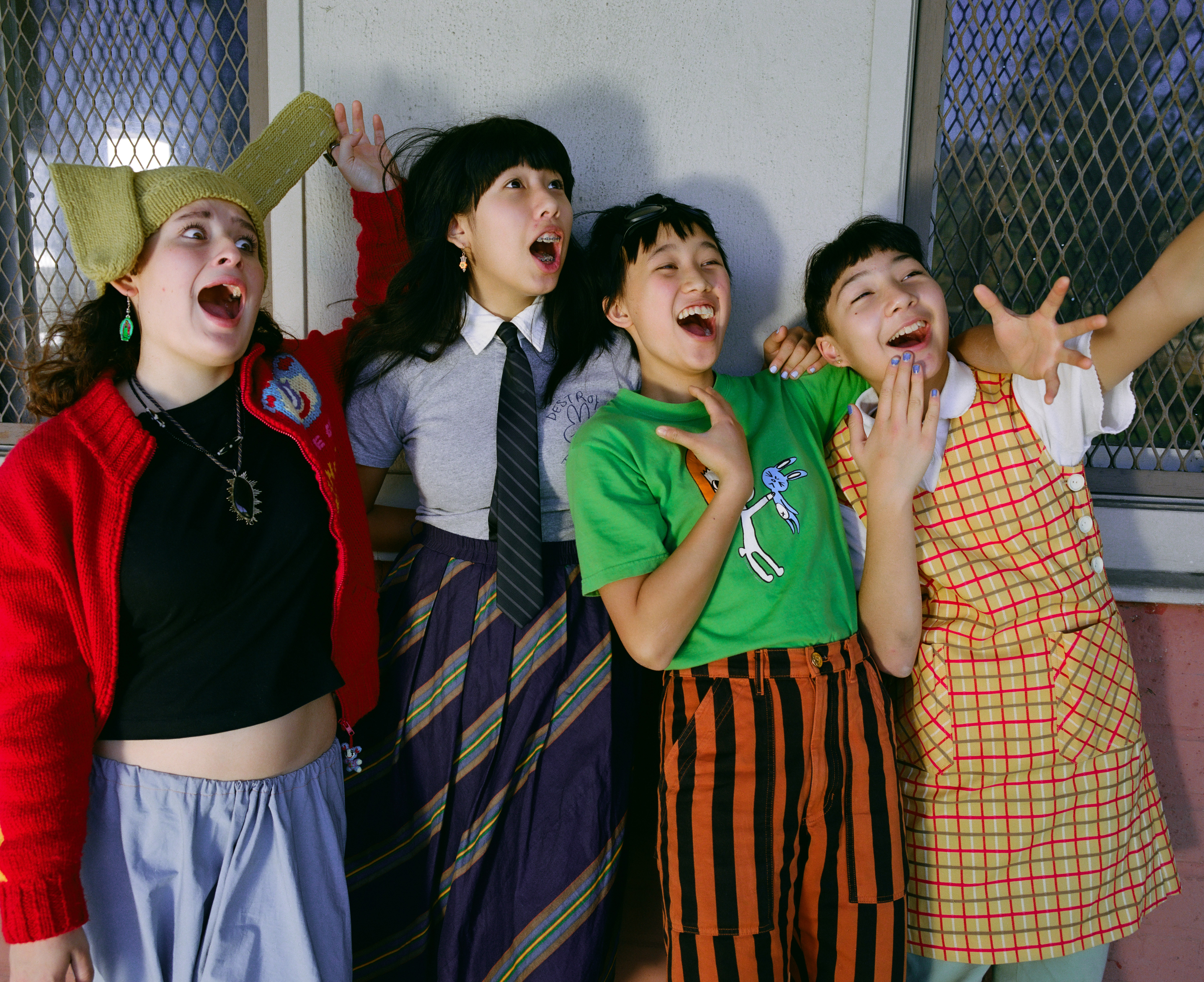 The Linda Lindas pull faces and do silly poses against a brick wall