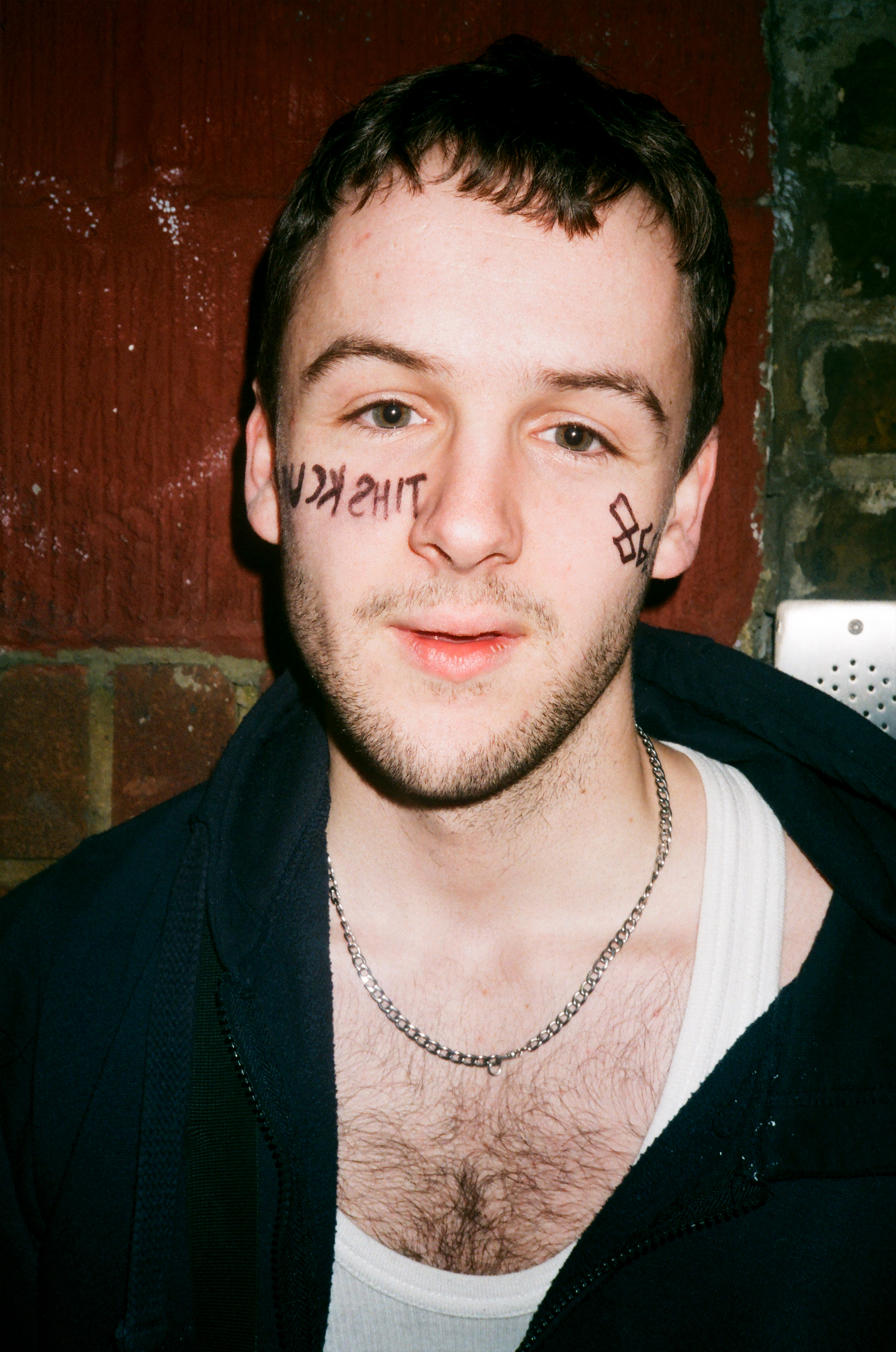 a brockhampton fan wearing a chain with drawn on face tattoos
