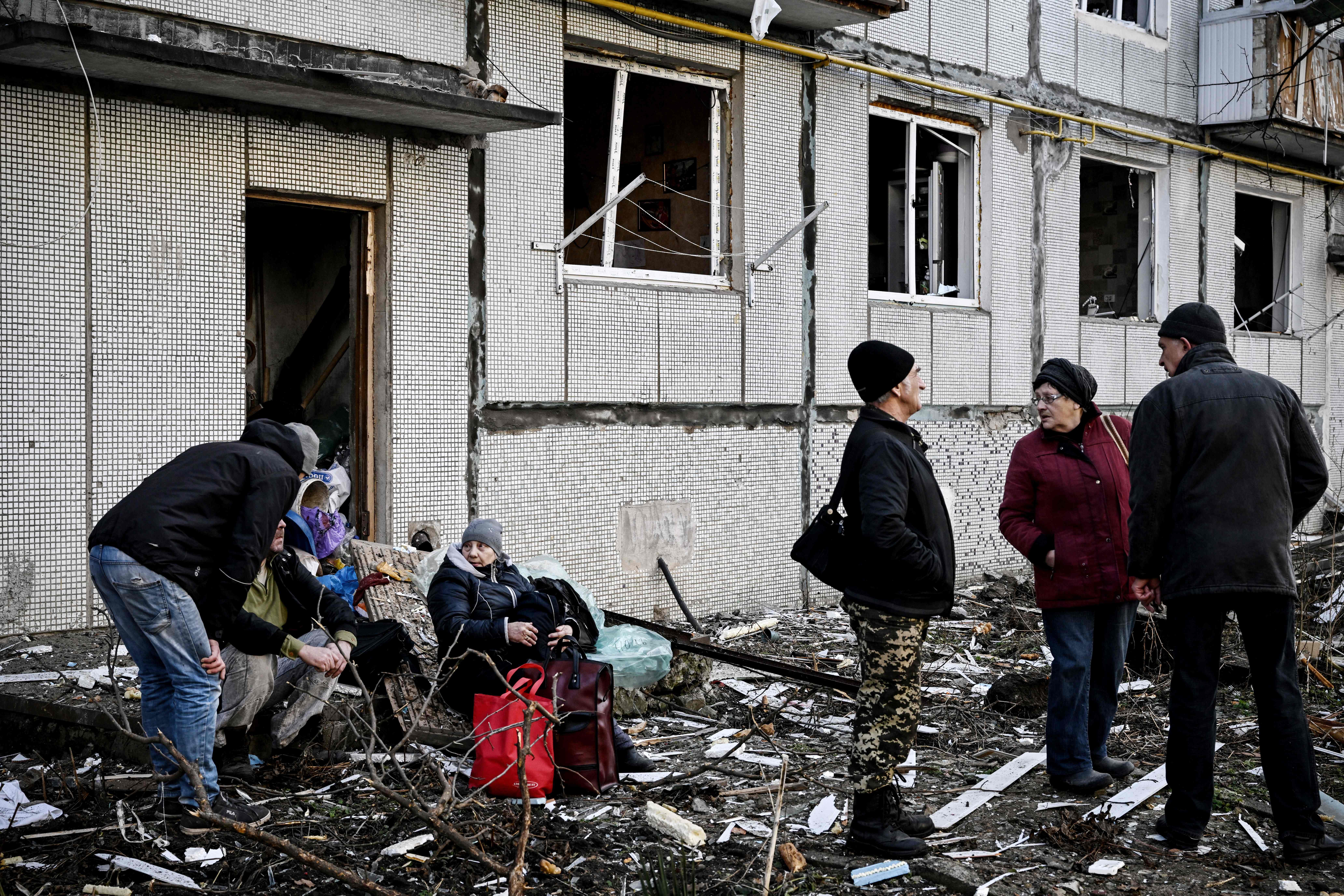 People stand outside a destroyed building after bombings on the eastern Ukraine town of Chuguiv on February 24, 2022