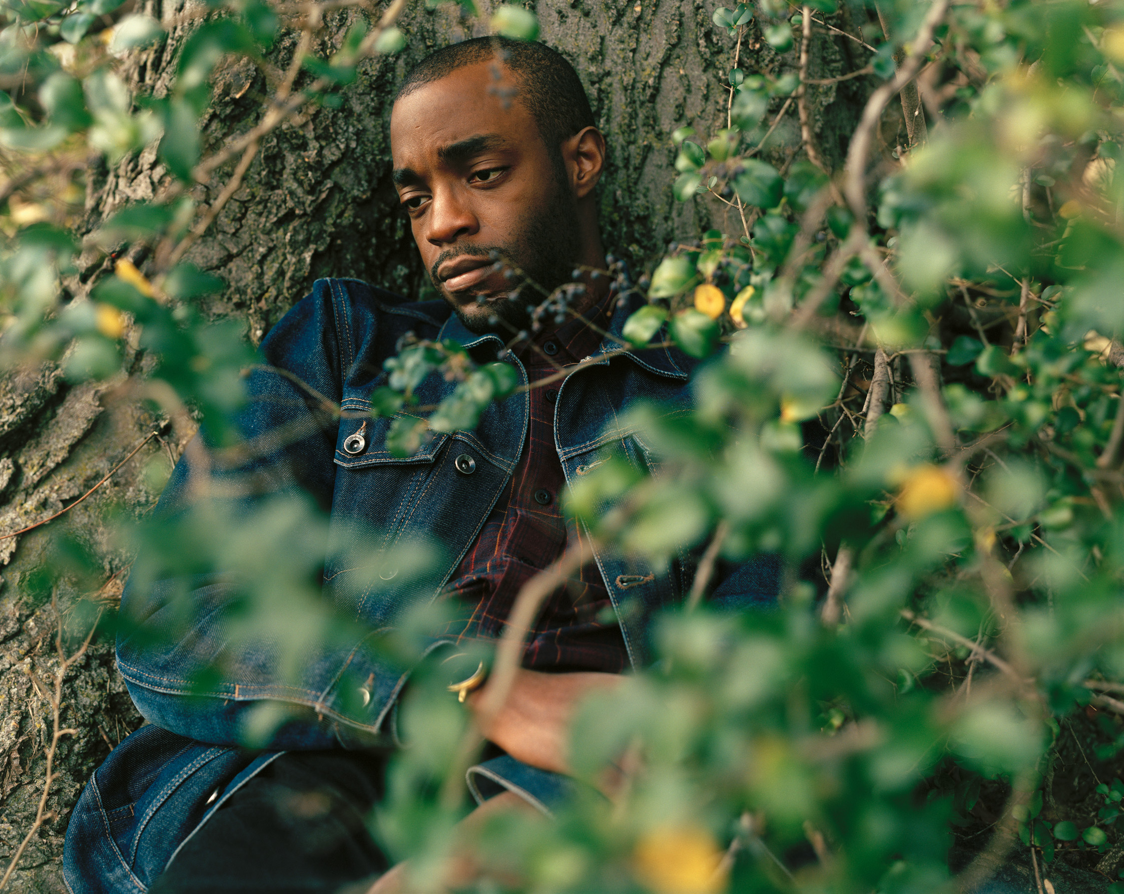 A man contemplating under a tree wearing a denim jacket