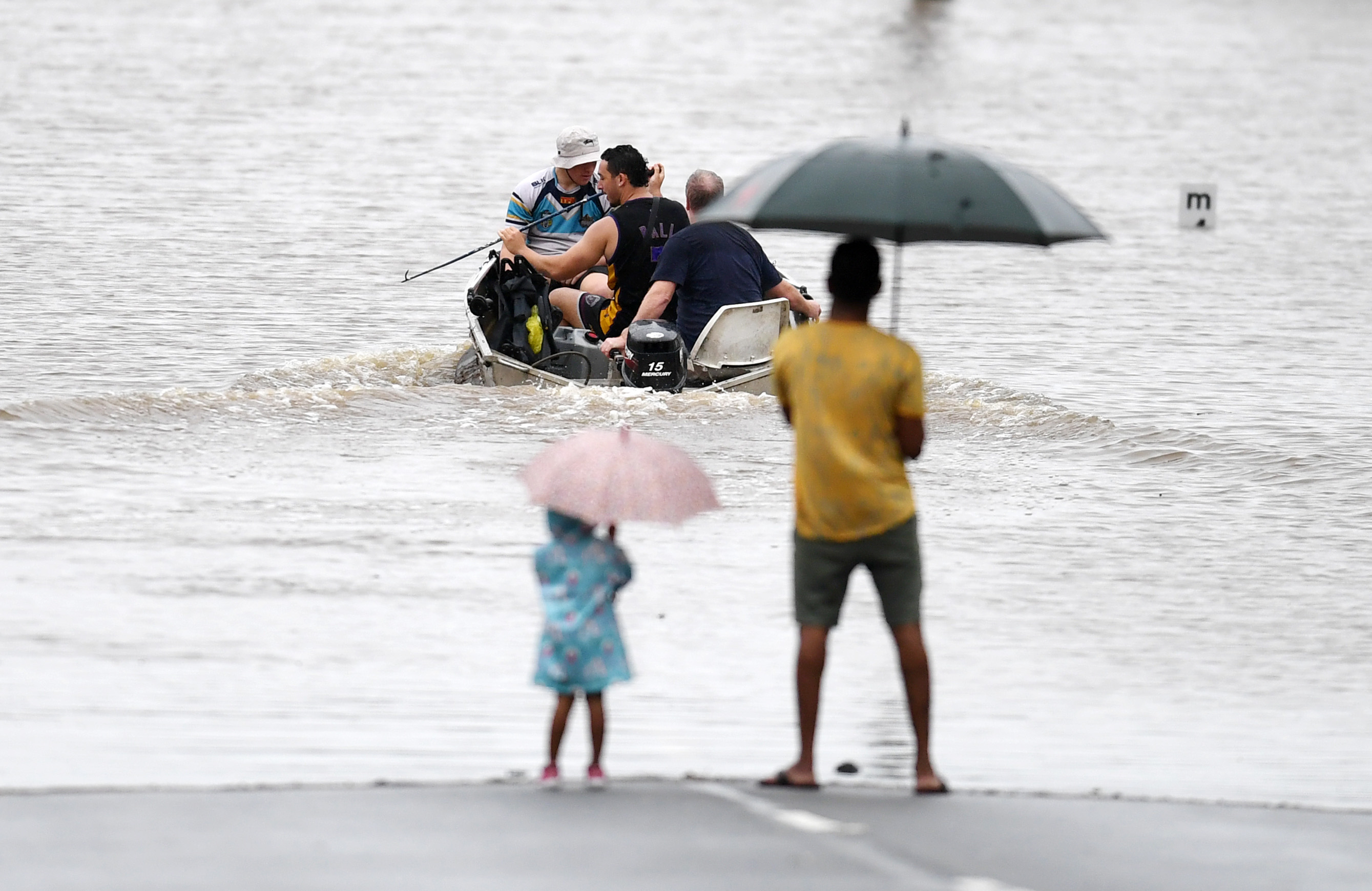 Seorang ayah dan putrinya menyaksikan warga mengarungi jalanan Logan yang banjir di wilayah tenggara Queensland. Foto: Dan Peled/Getty Images