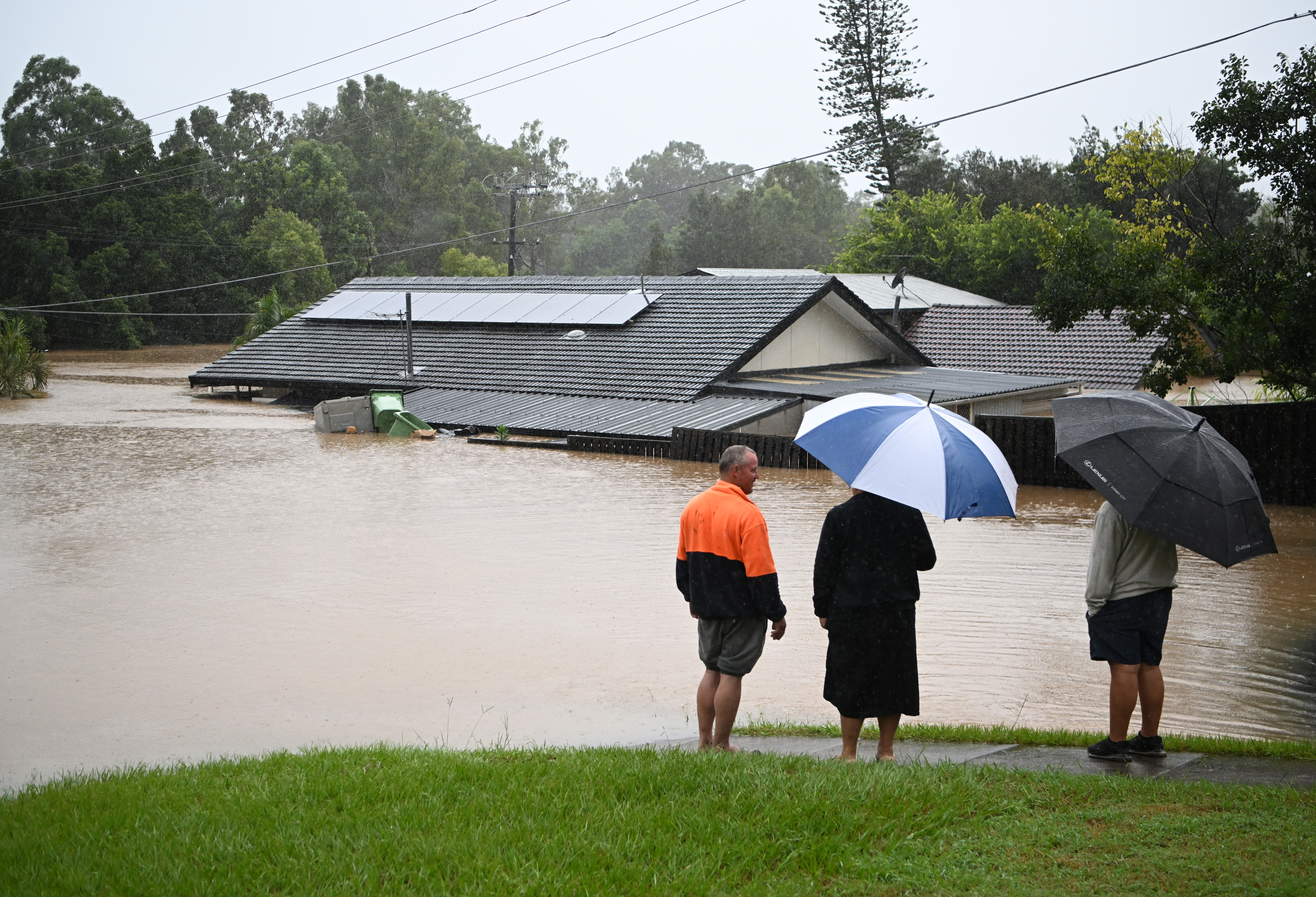 Tiga orang menghadap rumah yang terendam banjir di Goodna, Brisbane barat. Foto: Dan Peled/Getty Images