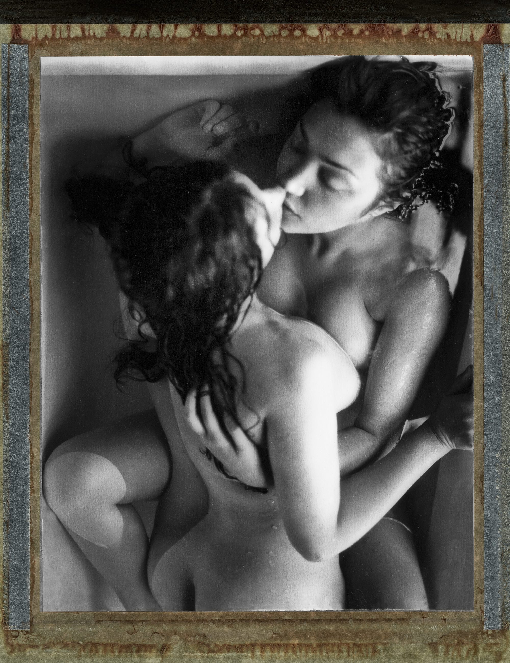 two women lie naked in the bath embracing and kissing