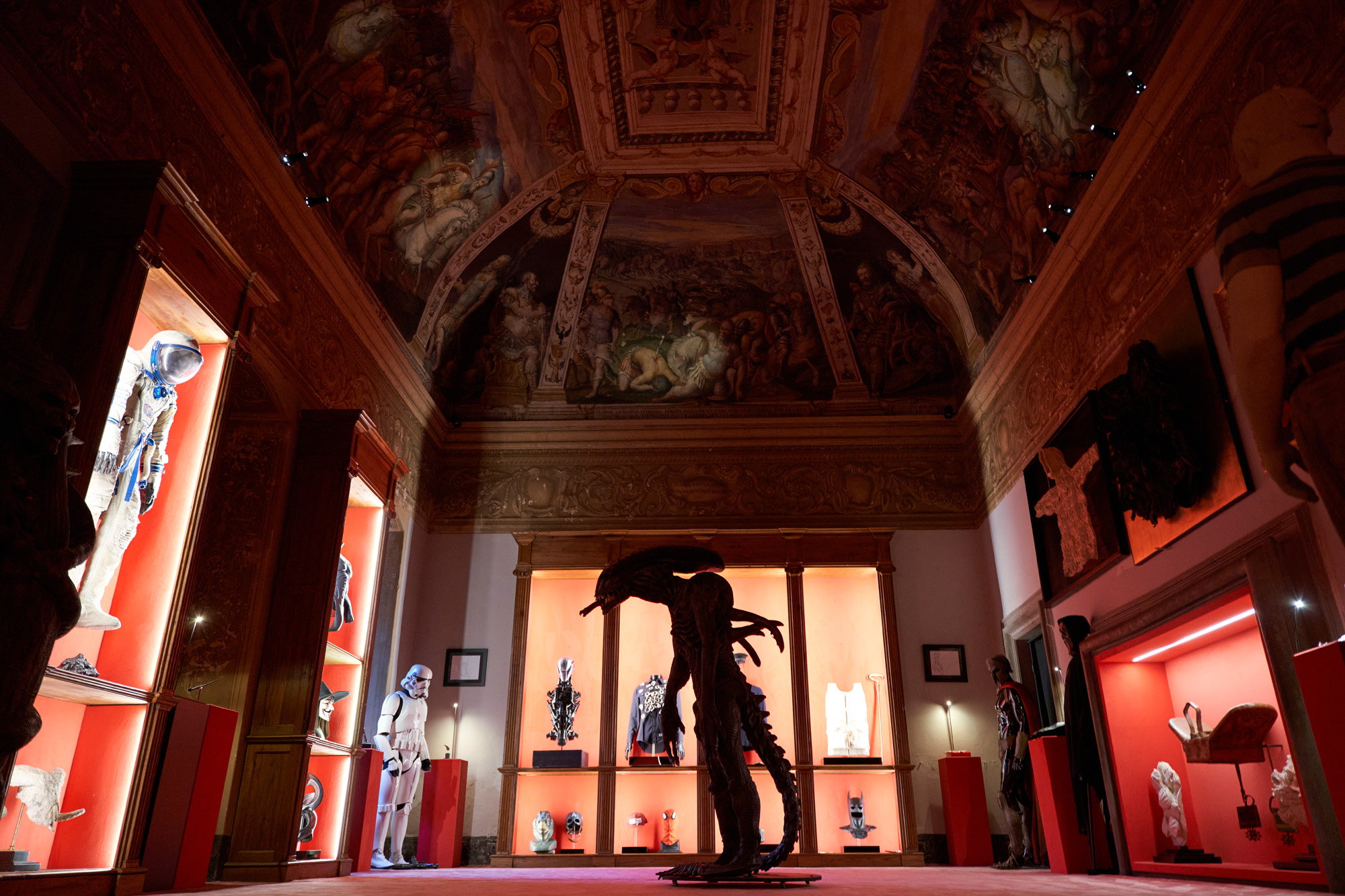 Ruangan galeri bernuansa merah dan putih memamerkan patung alien, karakter Star Wars dan baju astronot