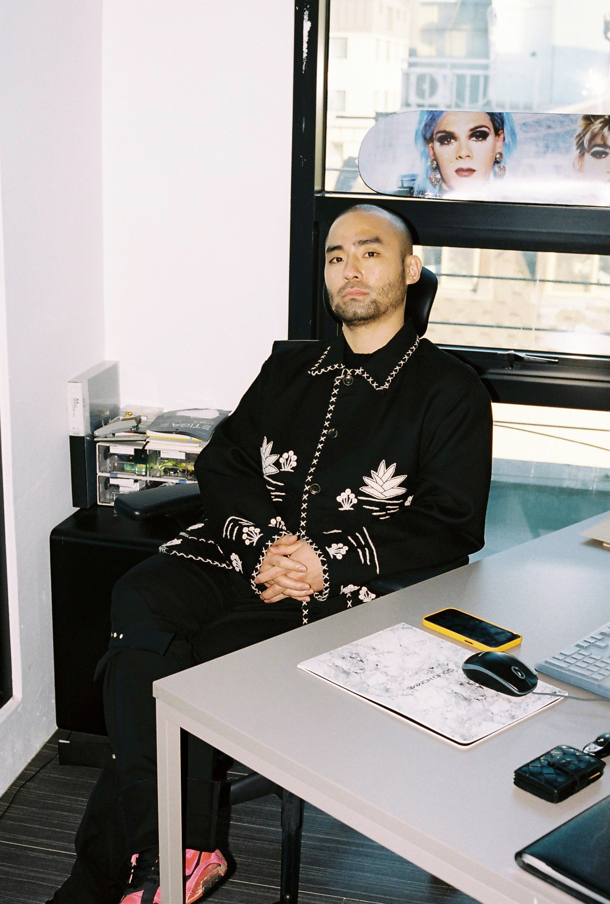 stylist youngjin kim sits behind his desk with a skateboard behind him 