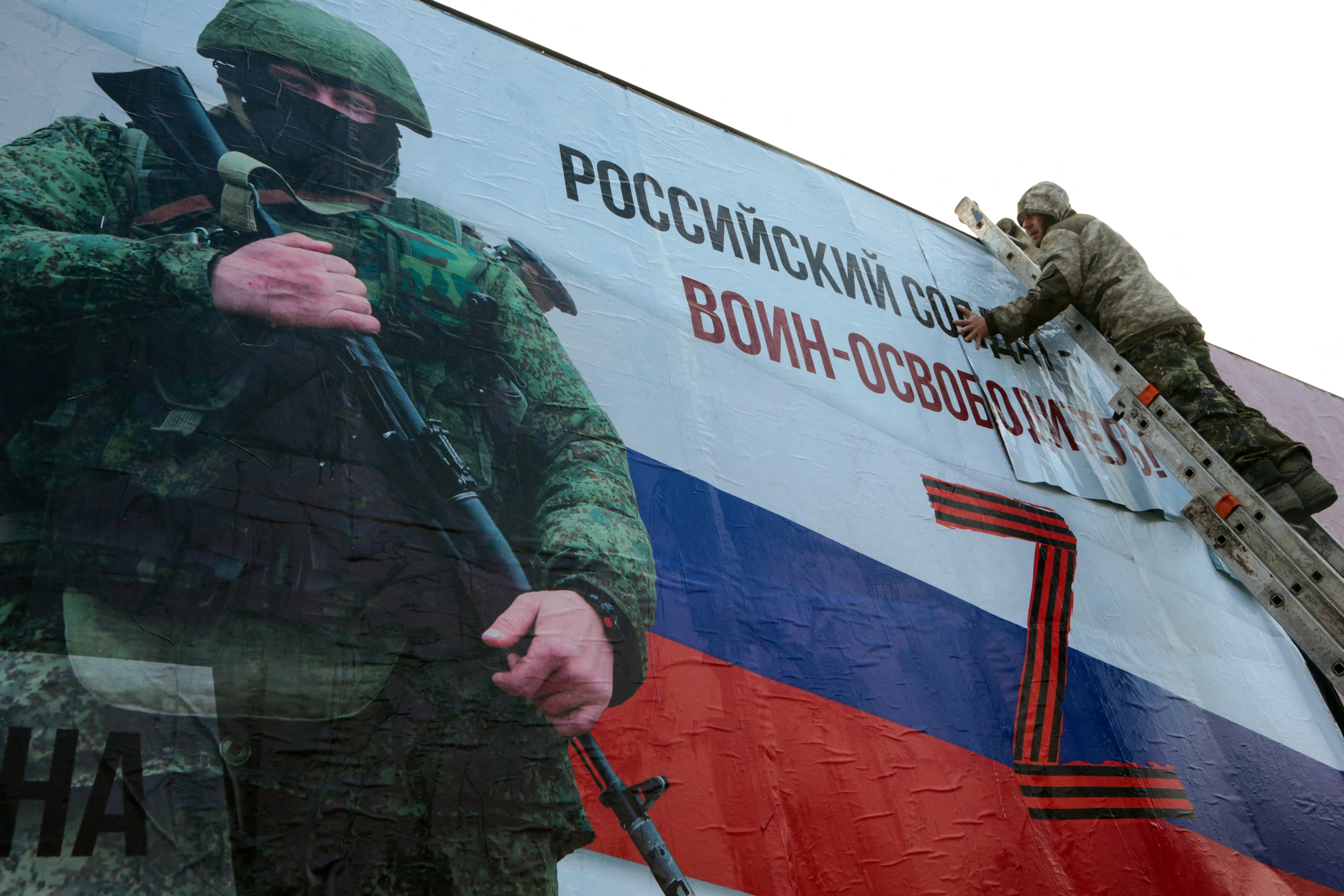 A man finishes glueing a huge placard depicting a Russian serviceman in the city center of Simferopol, Crimea, on March 4, 2022. The sign reads: “A Russian soldier is a liberator!” Photo: AFP/Stringer