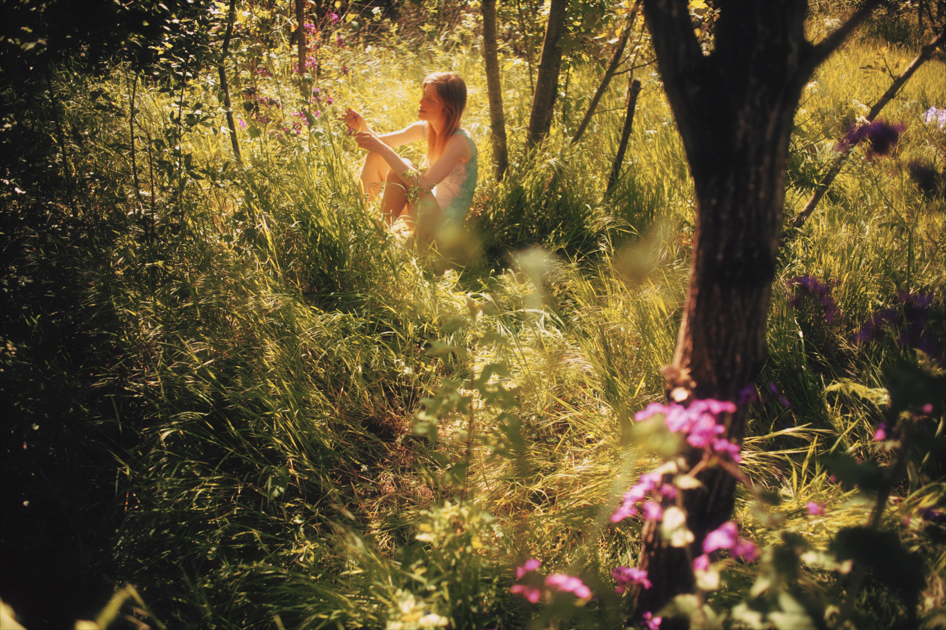 a woman in the grass surrounded by trees and flowers