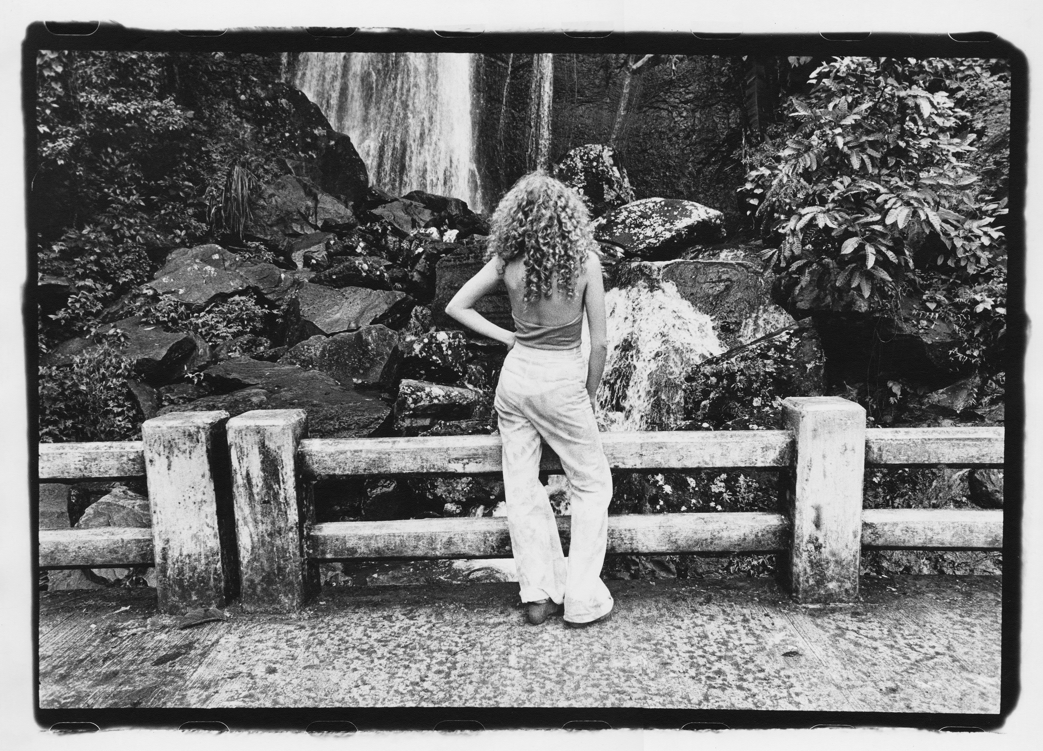 Photograph of a model standing with her back to the camera in front of a waterfall photographed by Marcia Resnick.