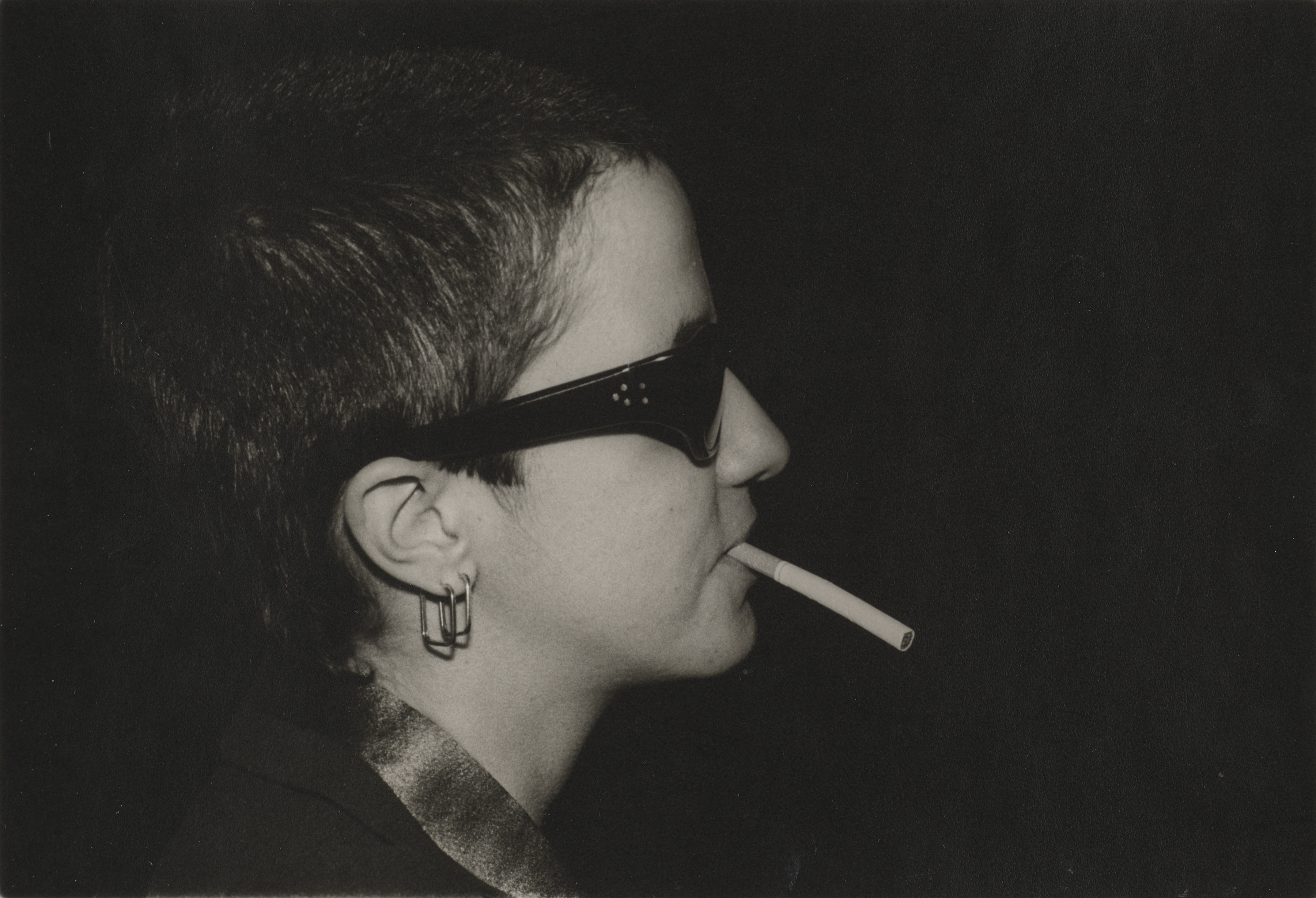 Photograph of Kathy Acker smoking and wearing sunglasses photographed by Marcia Resnick