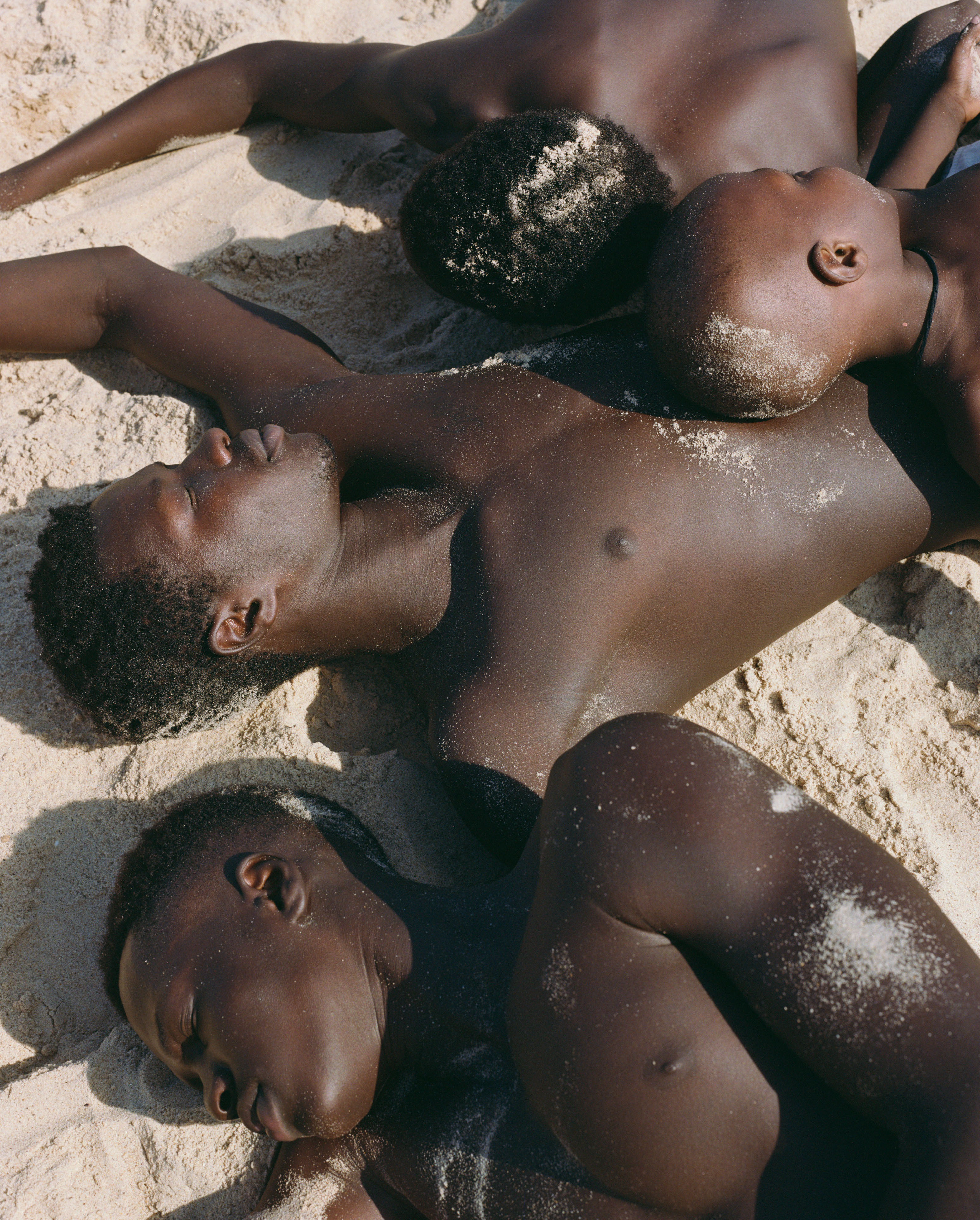 A group of young men lying in the sand on the beach.