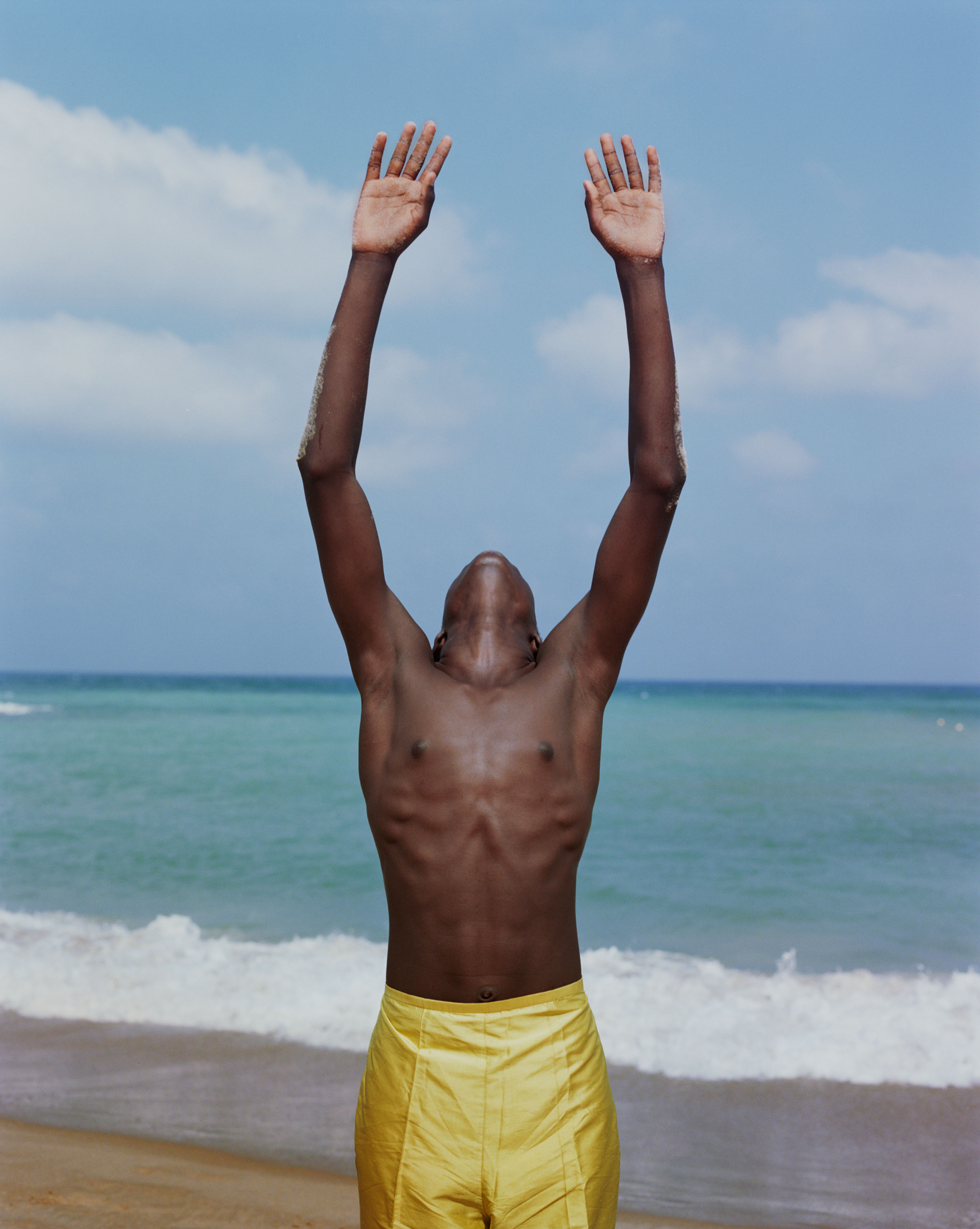 A man in yelloy pants on the beach looking up at the sky.