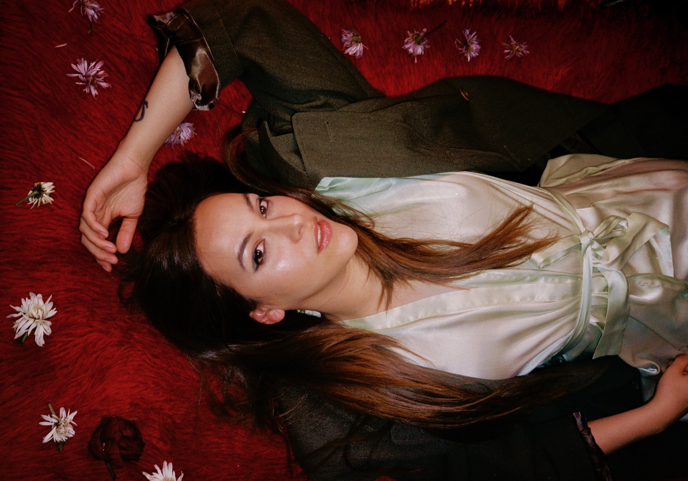 musican delia debit martinez lying on red carpet surrounded by flowers