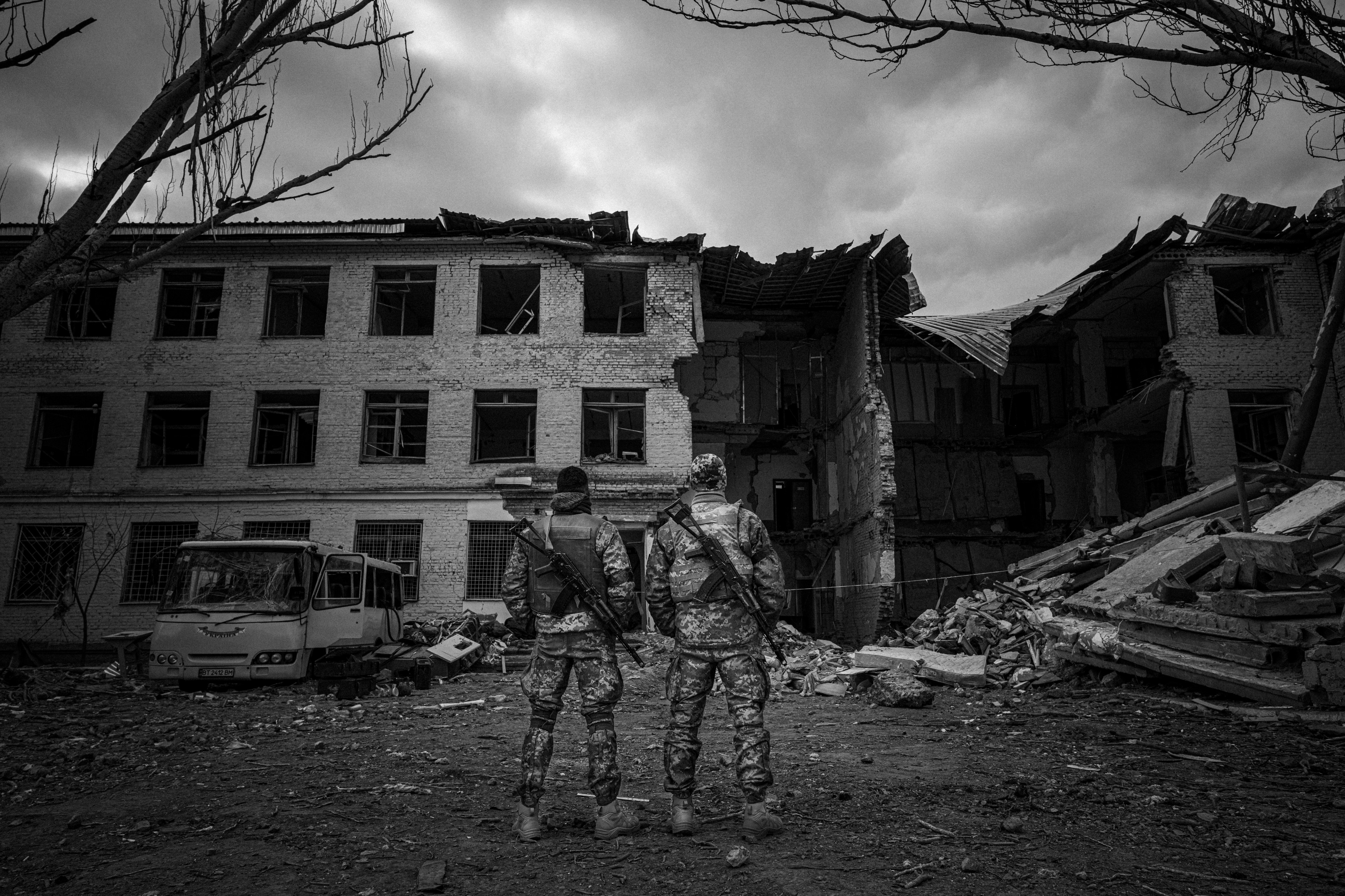 Dua prajurit berdiri menghadap pangkalan militer yang hancur akibat bom.