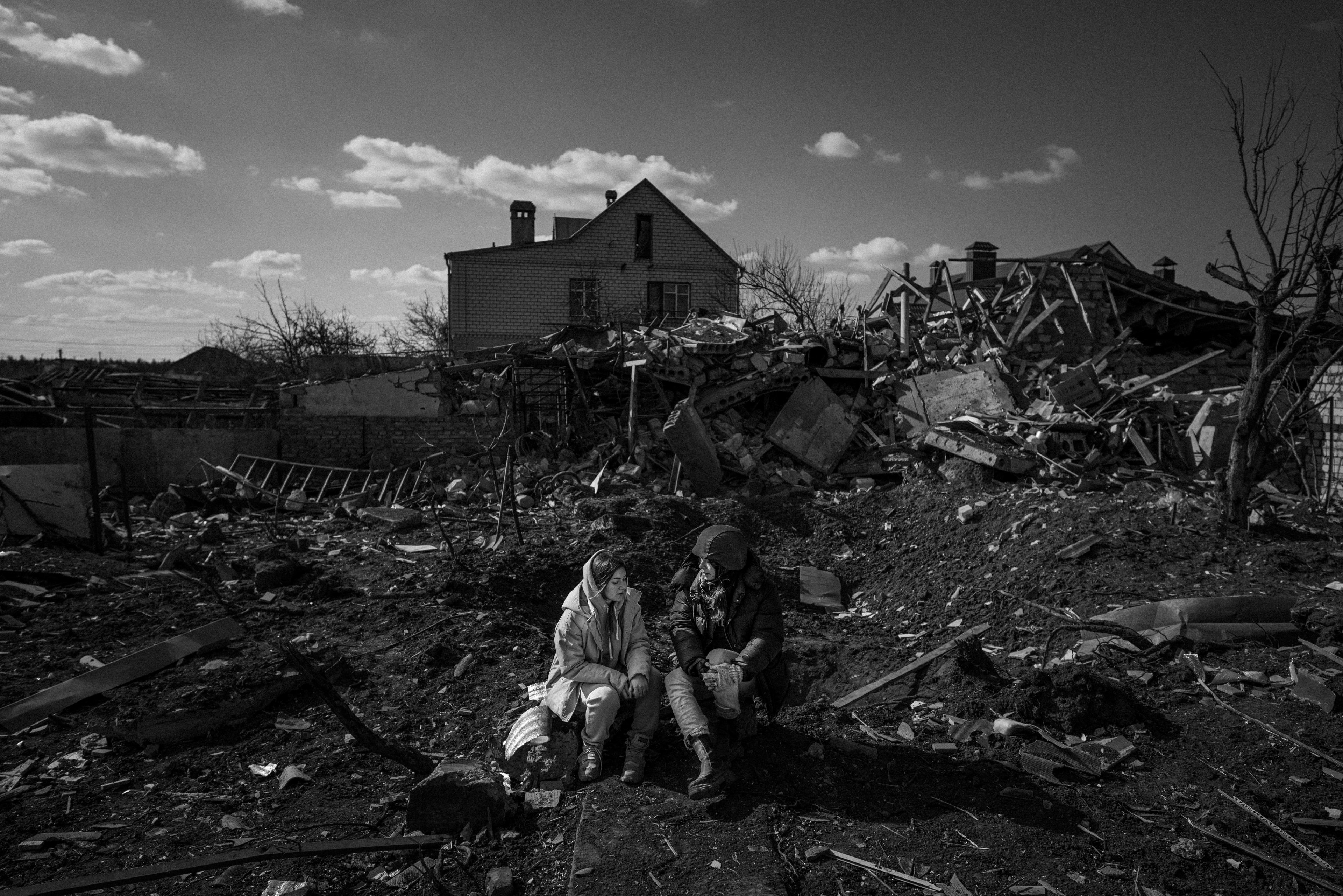 Dua perempuan duduk di sekitar reruntuhan bangunan