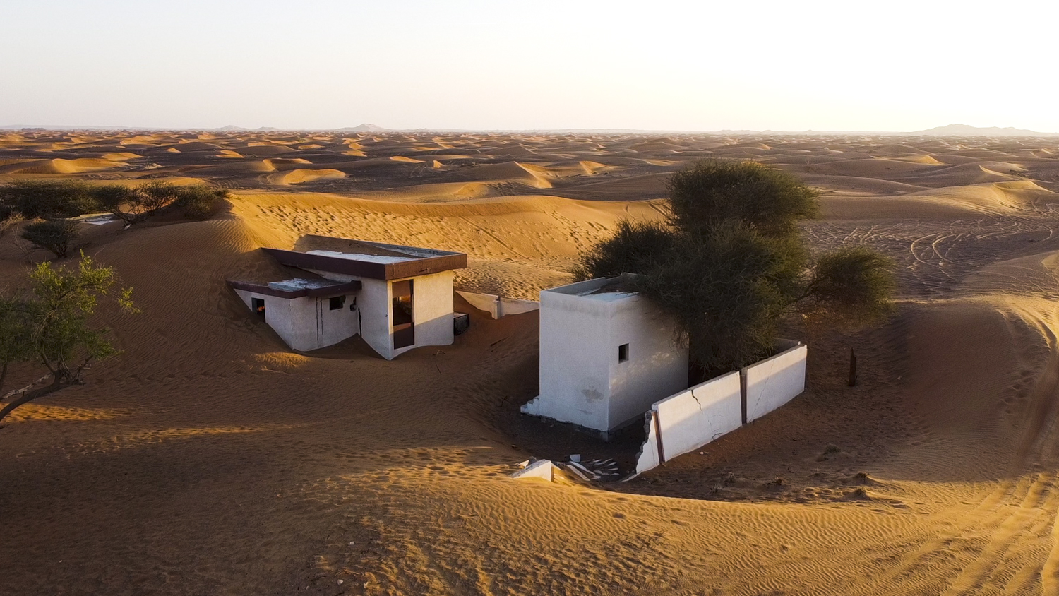 Dua rumah bertembok putih tertutup pohon dan pasir
