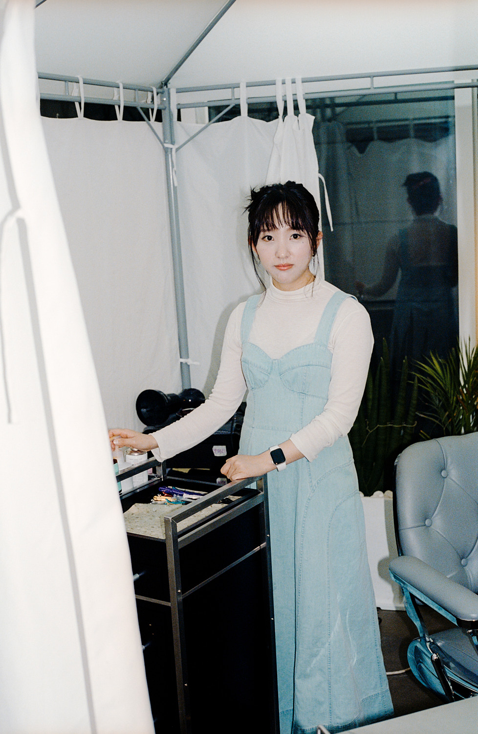 hair stylist jihee park stands in her salon wearing a denim dress
