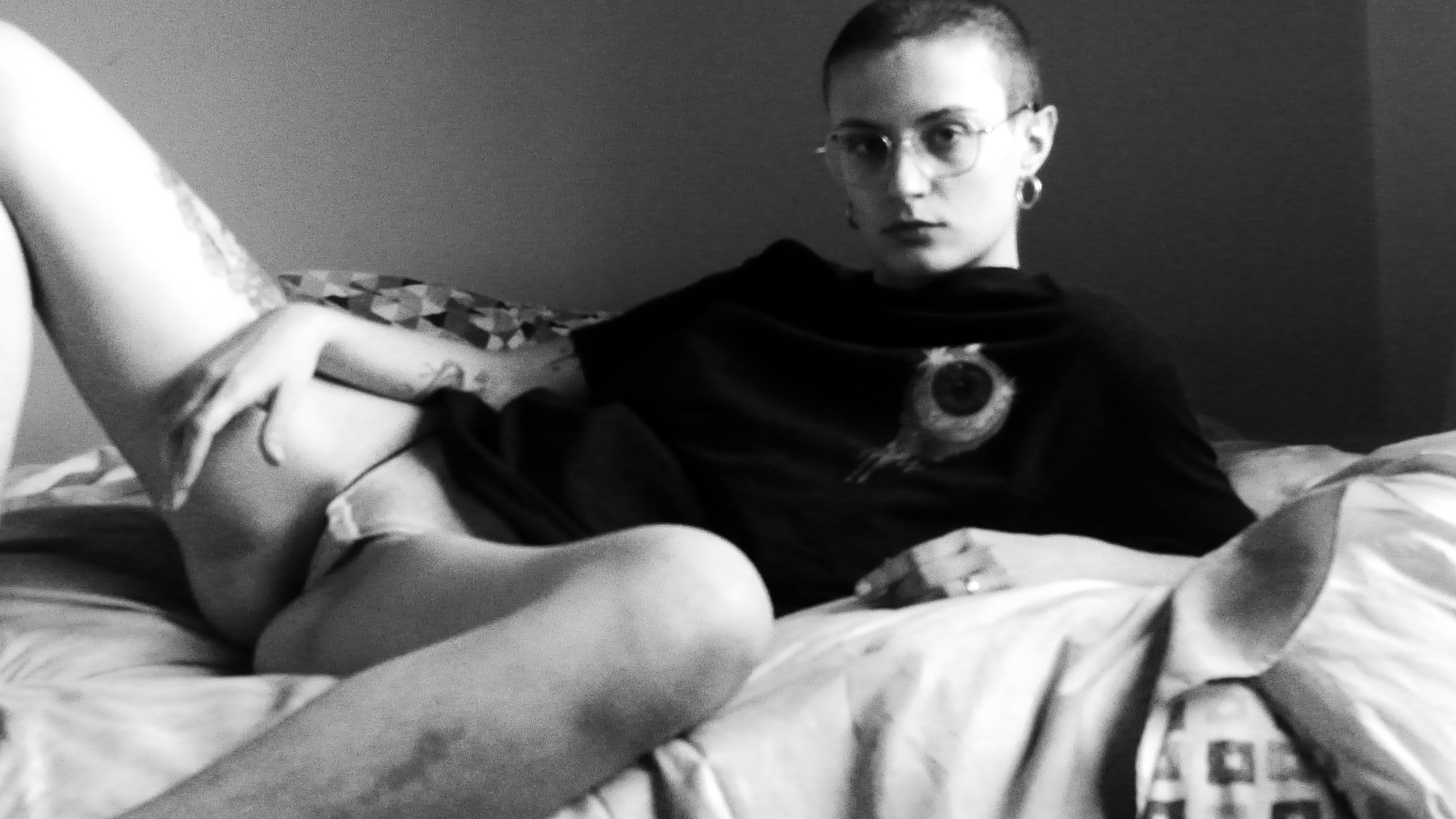 foto in bianco e nero di ragazza tatuata e rasata sdraiata sul divano con maglietta nera