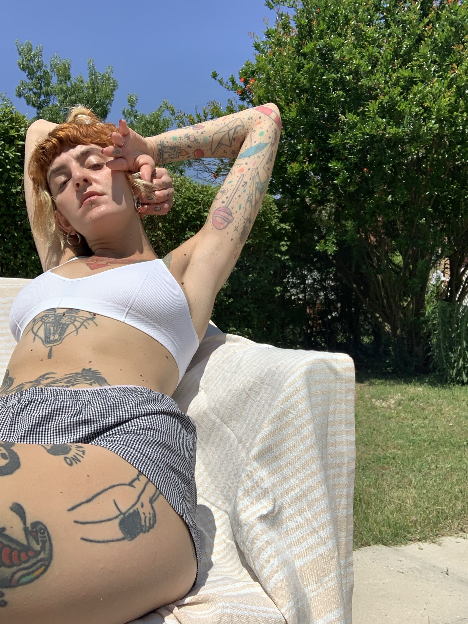 ragazza tatuata sdraiata in giardino sotto al sole