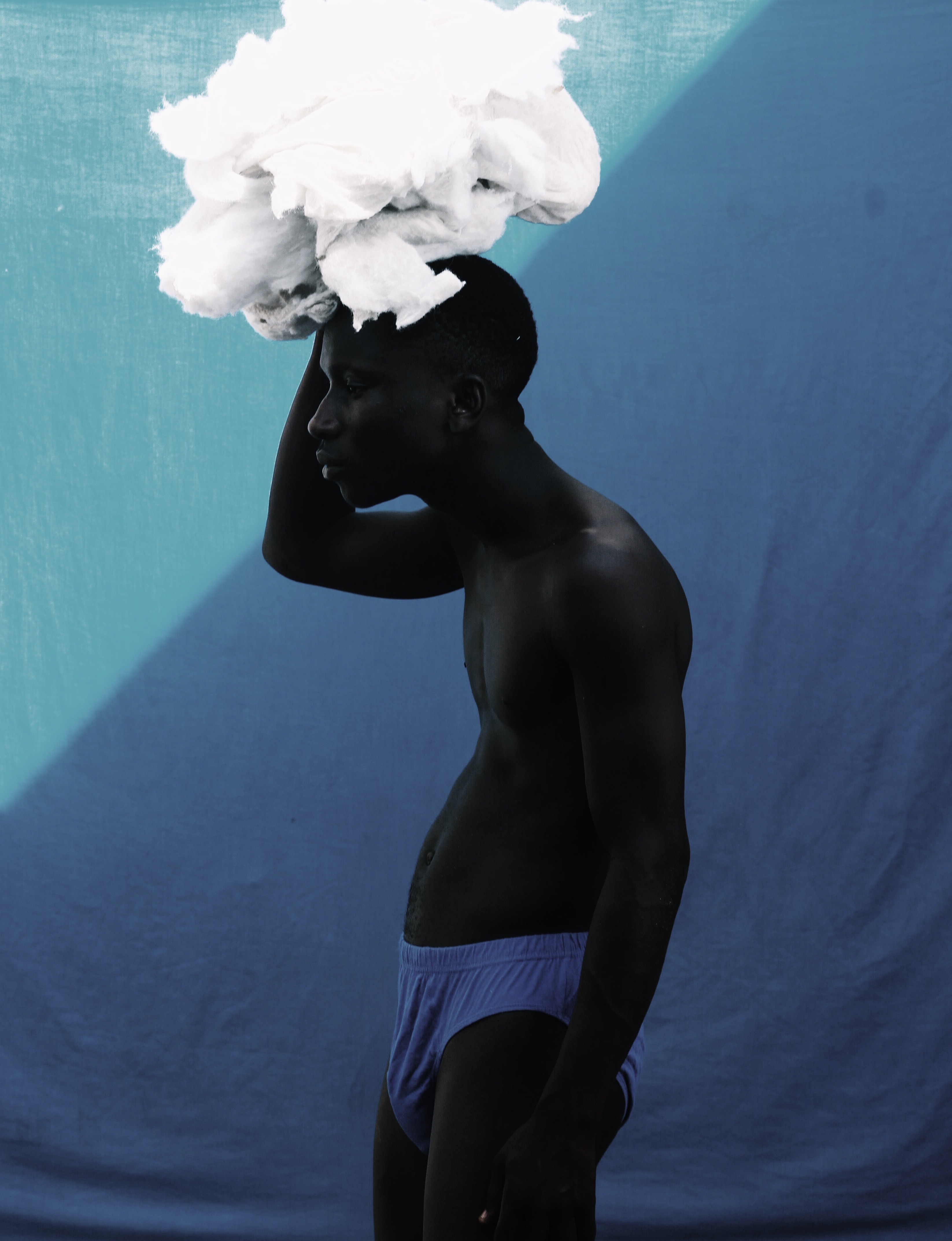 A young man in blue underwear carrying a cloud-llike bundle of fabric.
