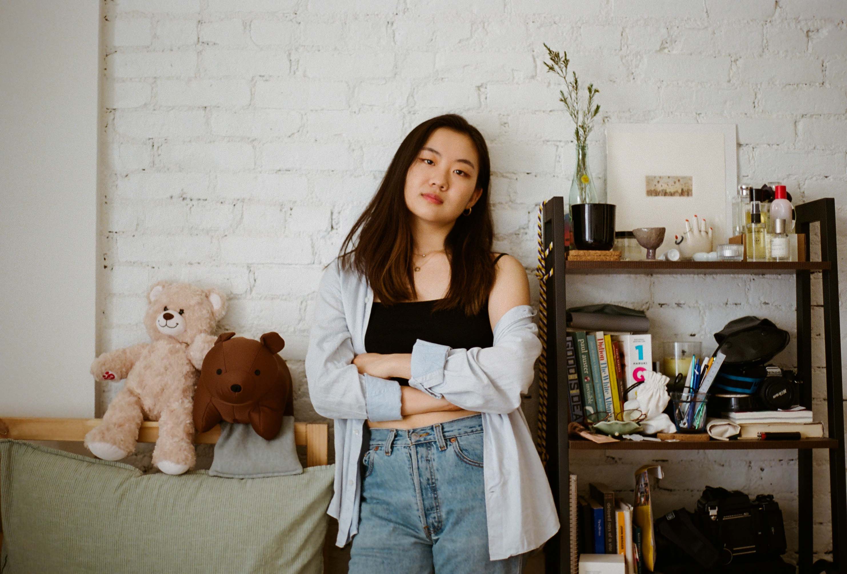 a portait of girl in her bedroom next to shelves with books and stuffed animals