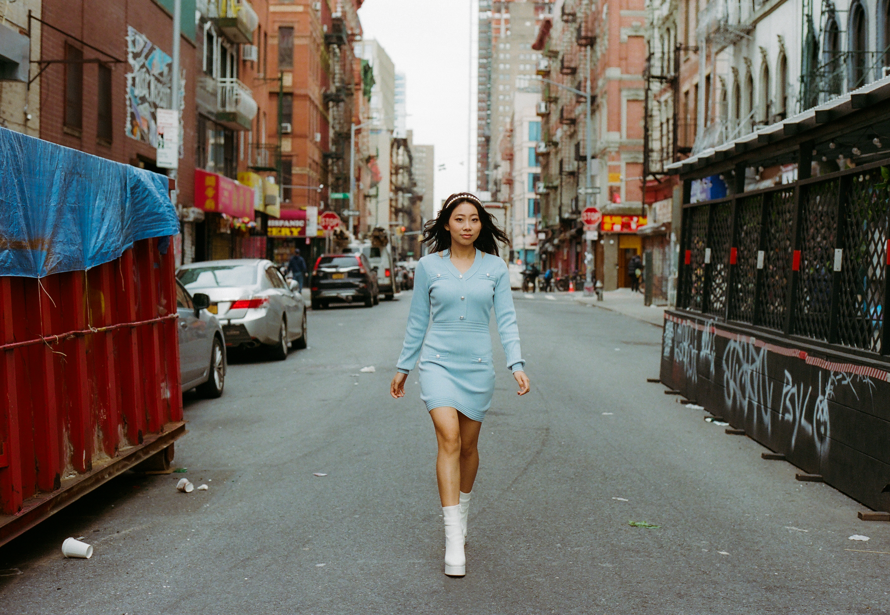 meg wearing a blue dress and white boots walking through new york's chinatown